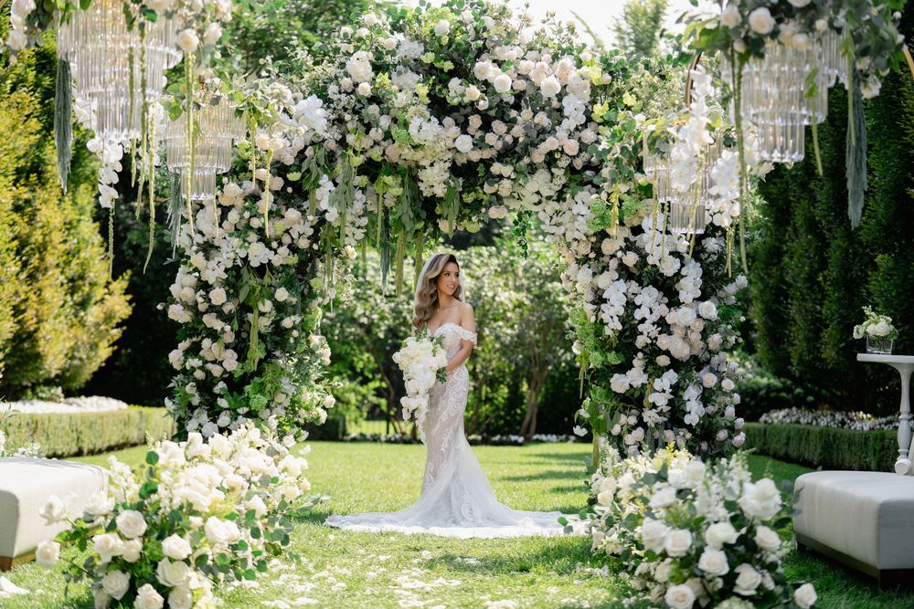 A beautiful white floral wedding arch adorned with roses and greenery stands elegantly in a garden setting.