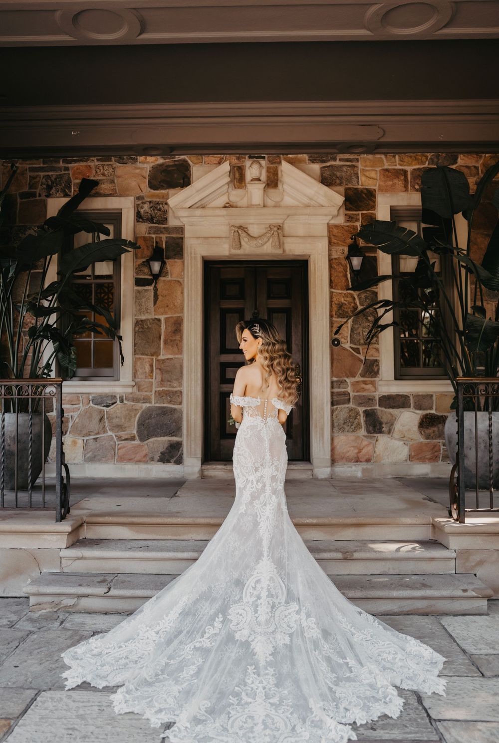 An ornate white wedding dress with a dramatic cathedral train displayed against a stone building facade.