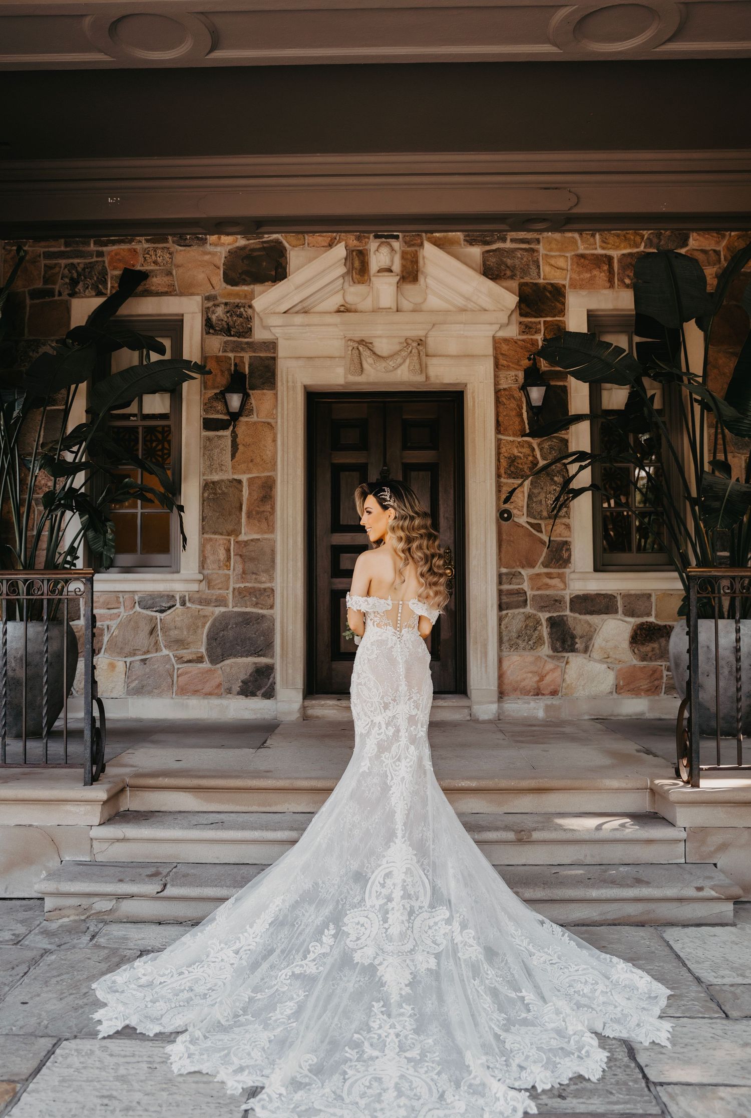 An ornate white wedding dress with a dramatic cathedral train displayed against a stone building facade.