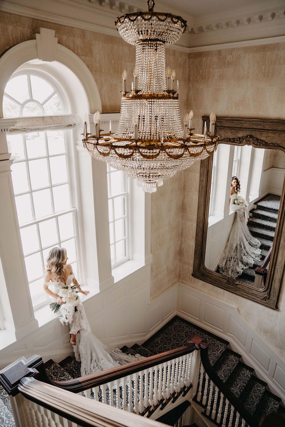 A grand staircase with crystal chandeliers and white walls creates an elegant wedding venue setting.
