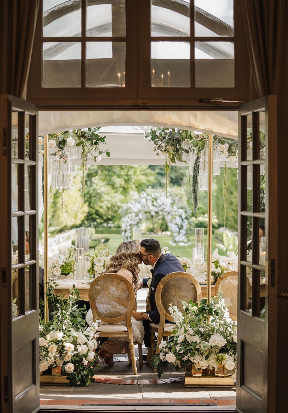 Wedding reception setup seen through window frames with natural greenery decorations.