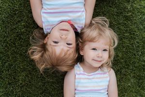 Sbilings in a striped shirt lies on green grass with their hair spread out in a playful pose during a family photoshoot in Sydney Rouse Hill