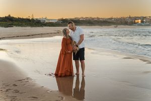 Two figures embrace on a sandy beach at sunset with golden light reflecting off the ocean waves.