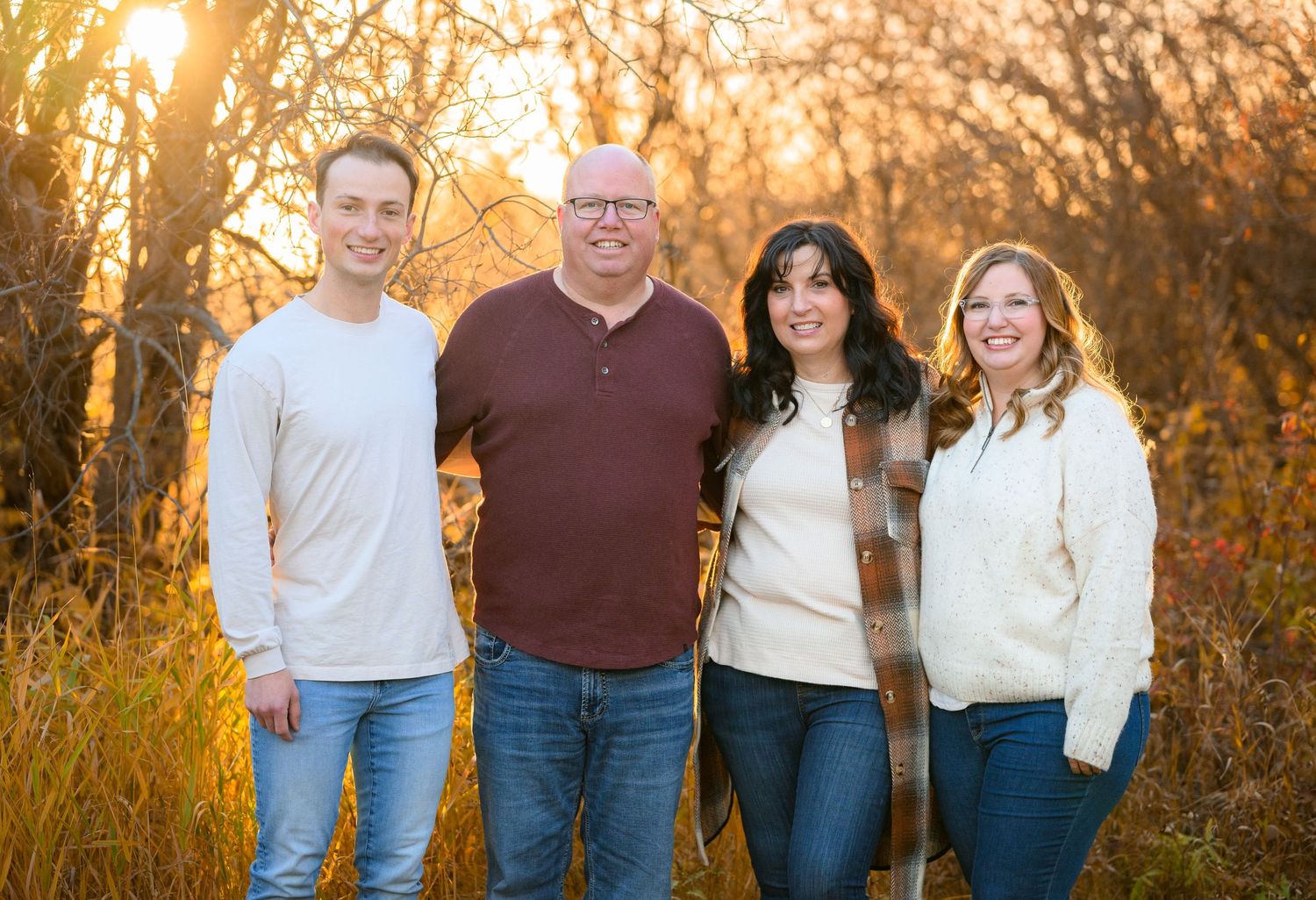 A group of four people stands together outdoors against a golden autumn sunset background in matching casual attire.