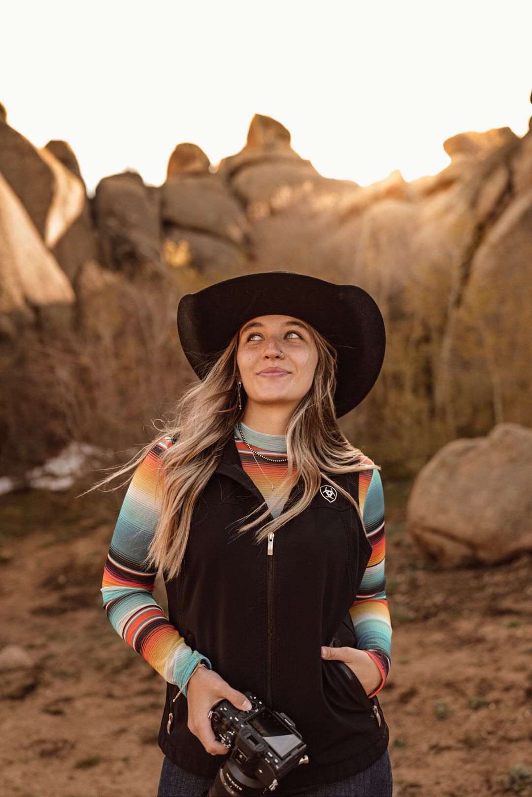 Person in black sweater holding a drink bottle against sunset sky with trailer in background.