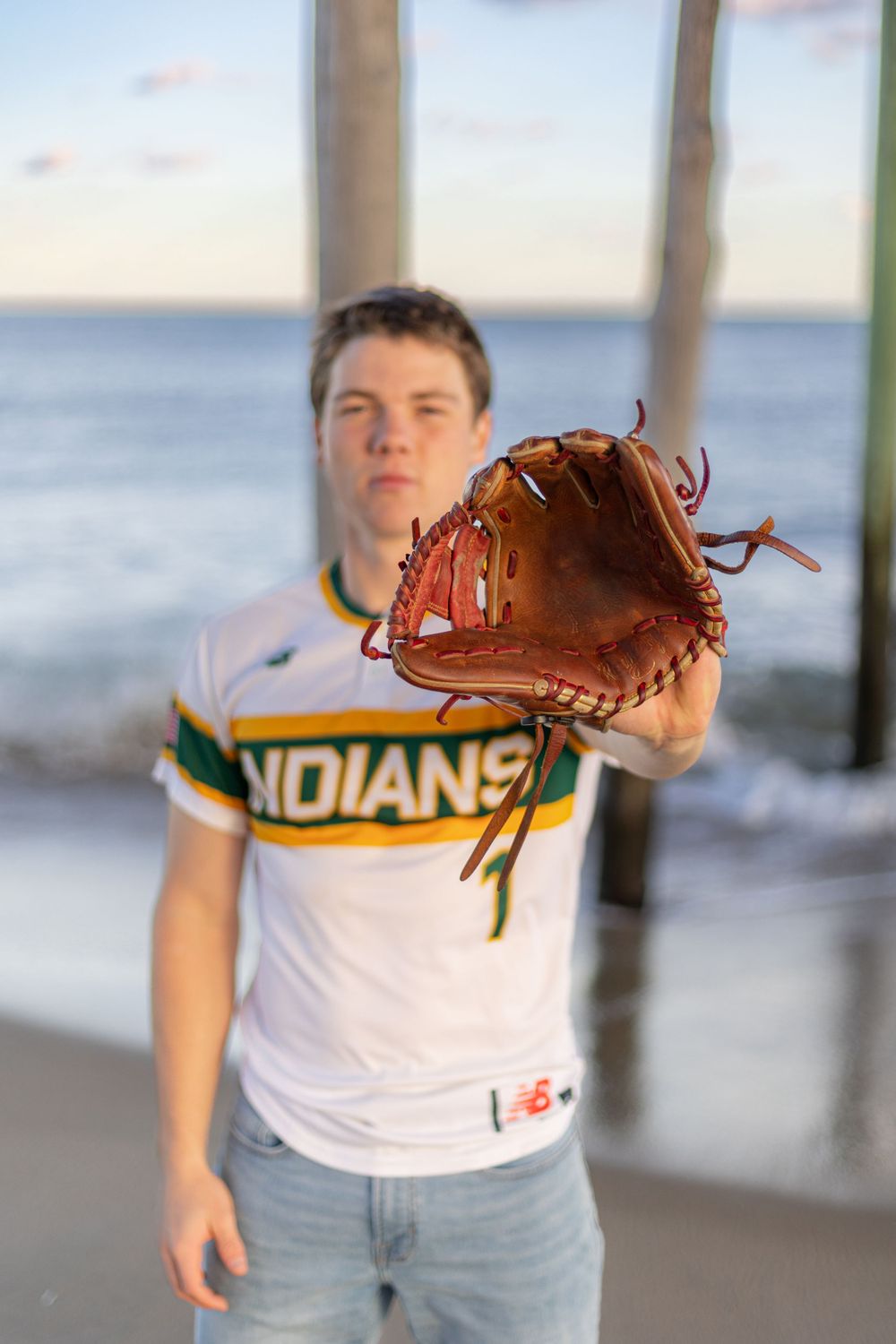 Baseball player displays leather glove while wearing Indians jersey under pier.