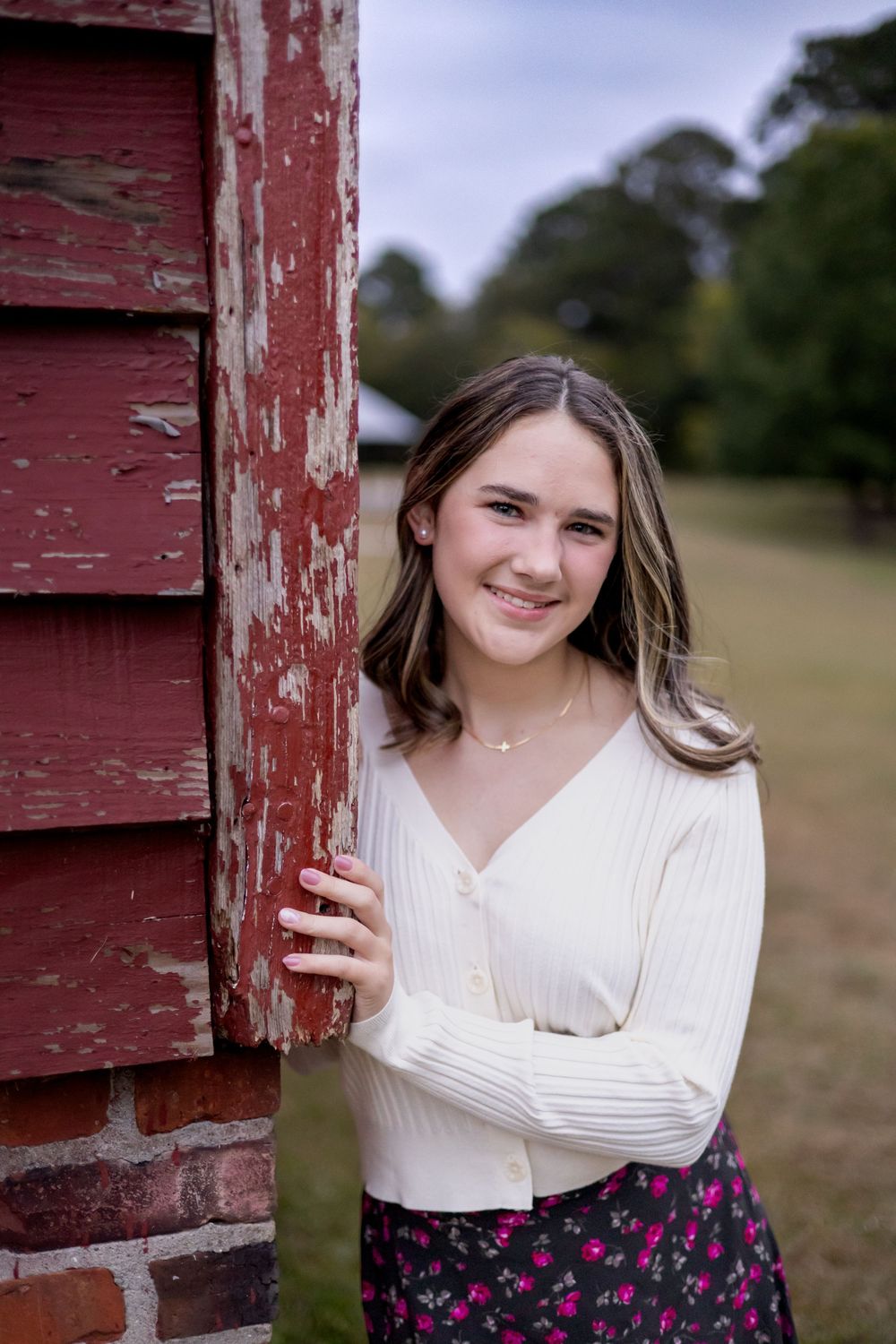A series of portrait photos taken against a rustic red barn wall showing someone in a white sweater with floral skirt.