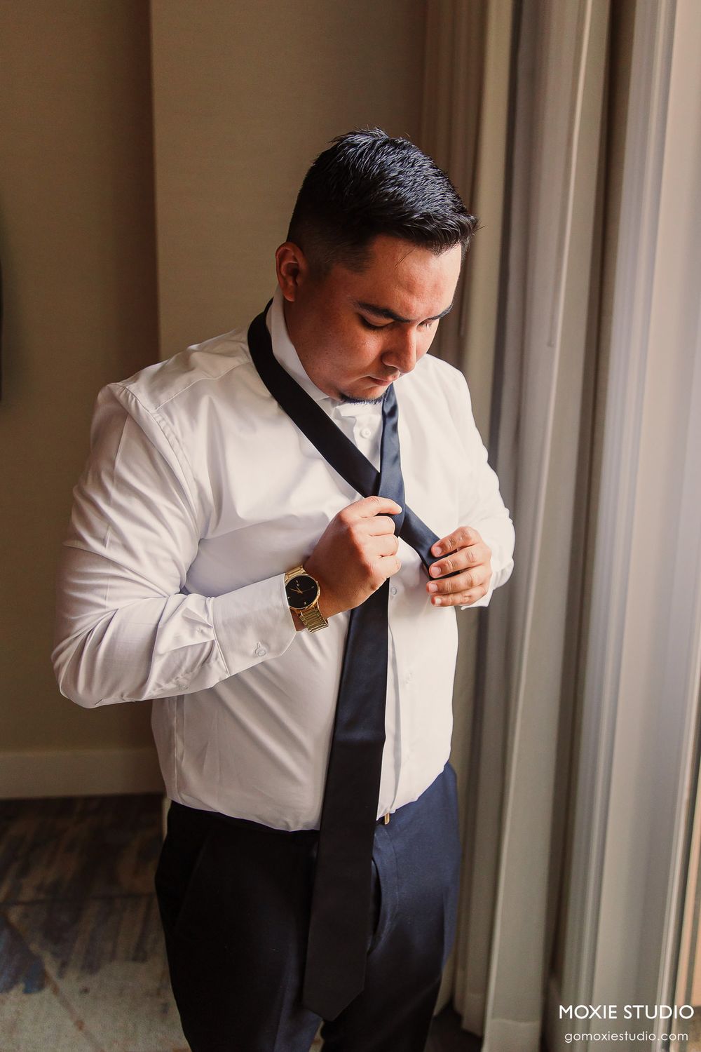 Series of photos showing someone adjusting their tie while getting dressed in formal attire by a window.