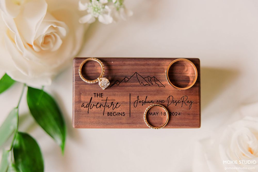 Wedding rings rest on a rustic wooden box surrounded by delicate cream roses and greenery.