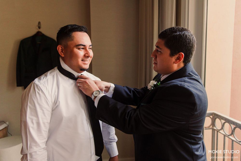 Two people in formal attire stand in conversation near an ornate railing in an elegant indoor setting.