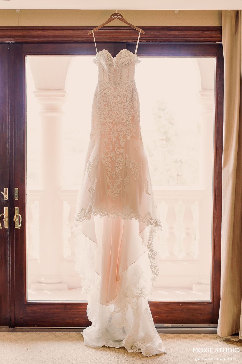 Beautiful white lace wedding dress hanging in front of a window with natural light streaming through.