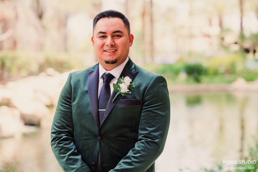 Groomsmen in dark suits and ties stand together for formal wedding portraits in an outdoor garden setting.