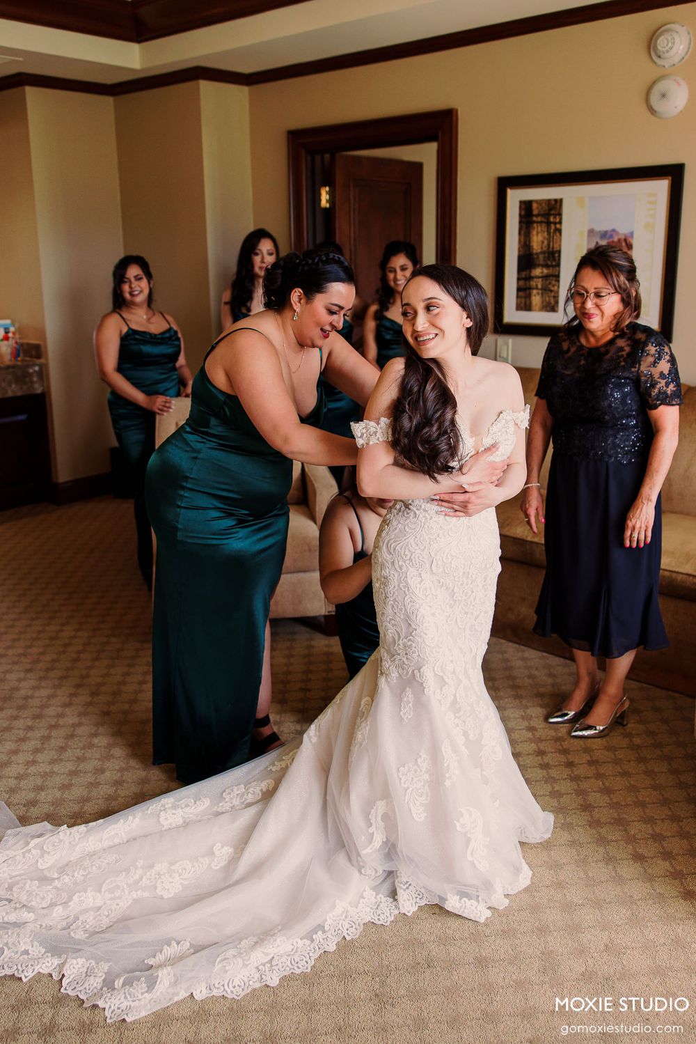 Wedding party in dark teal dresses and white gown dancing and celebrating in a hotel hallway.