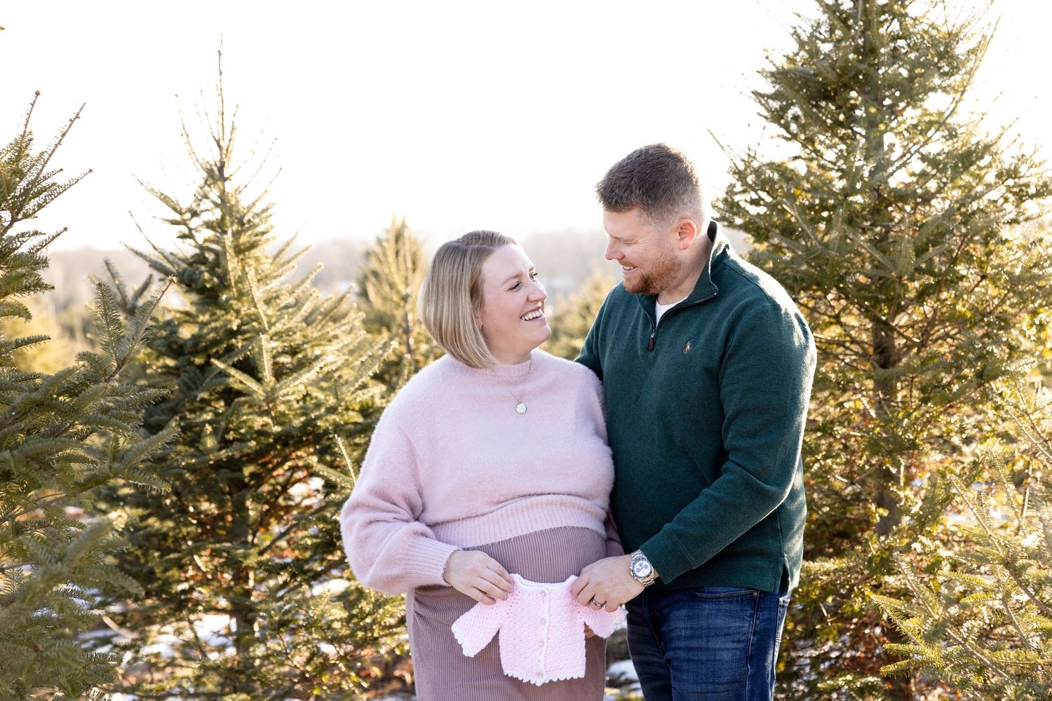 Romantic maternity photos among evergreen trees at sunset.