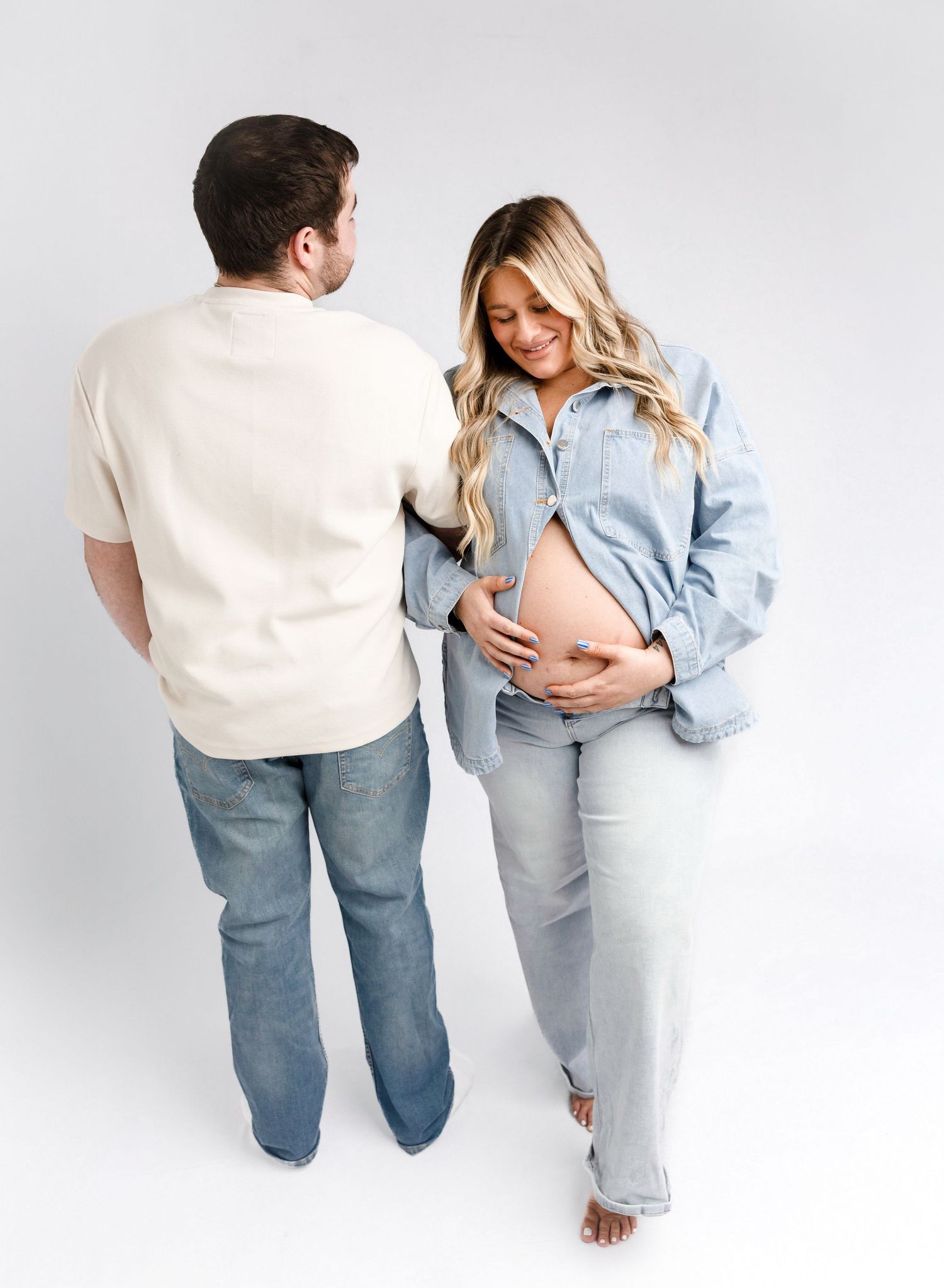 Couple in casual denim outfits embracing against white background.