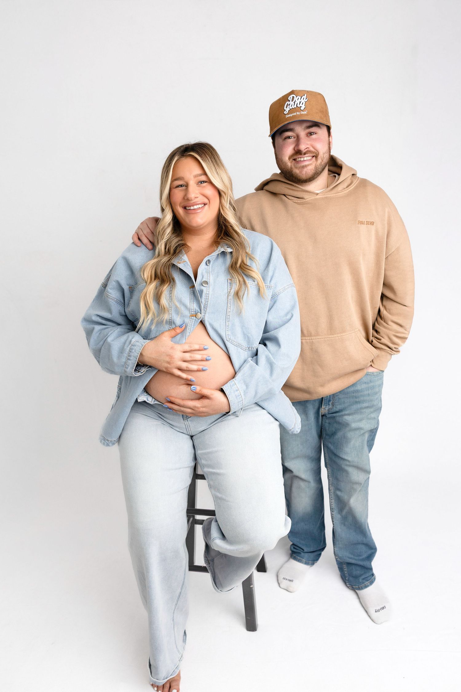 Casual maternity photoshoot with couple in denim and neutral tones.