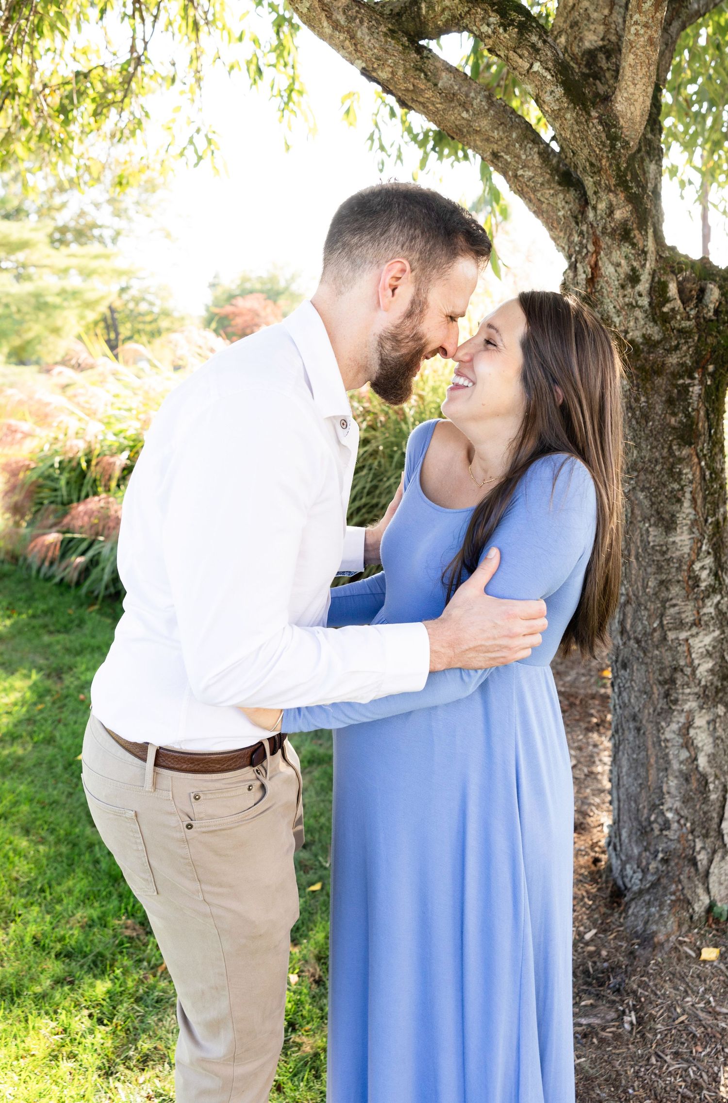 Romantic maternity photos under willow tree with couple in blue dress and white shirt.