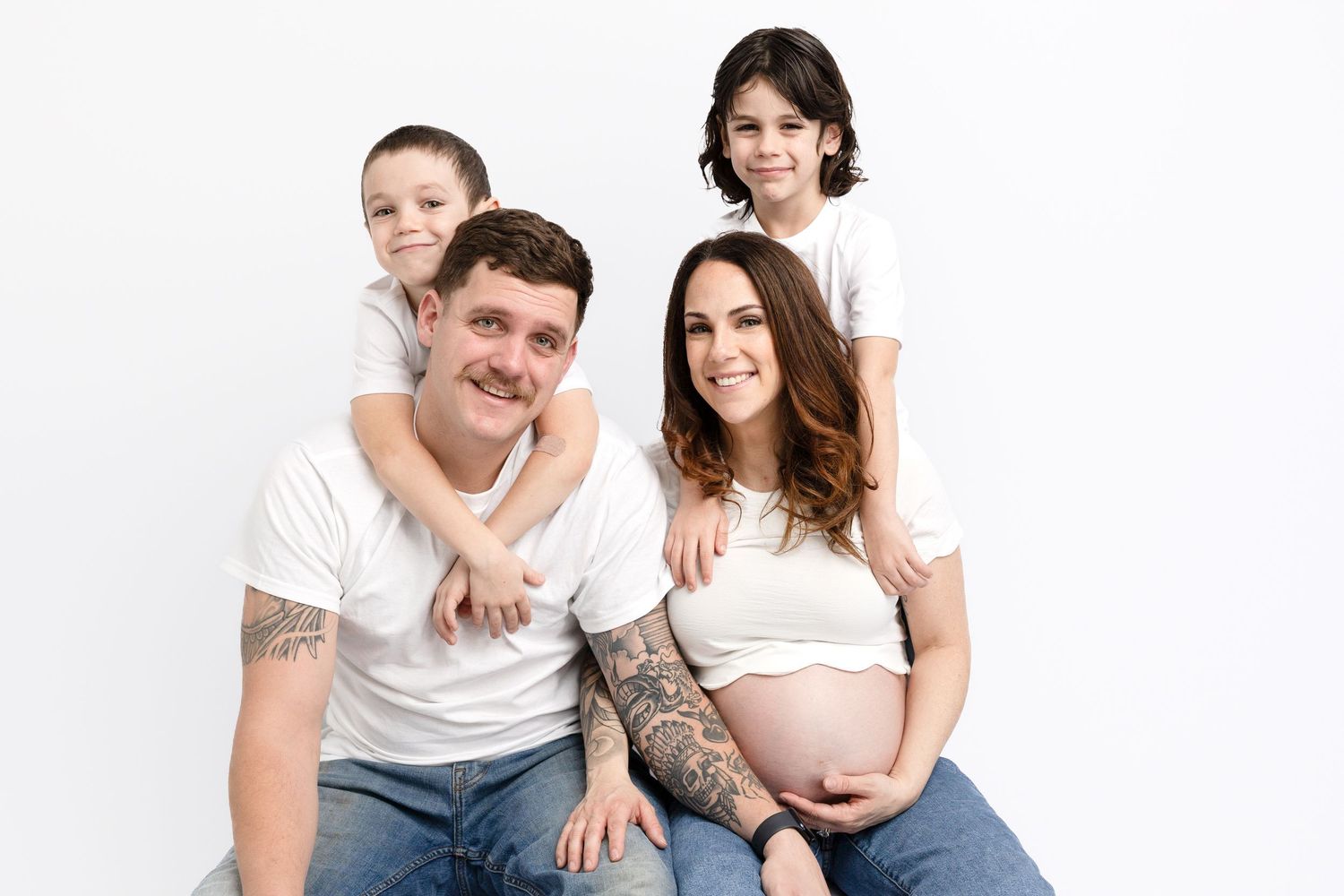 Family photo session on white background wearing coordinated white tops and blue jeans.