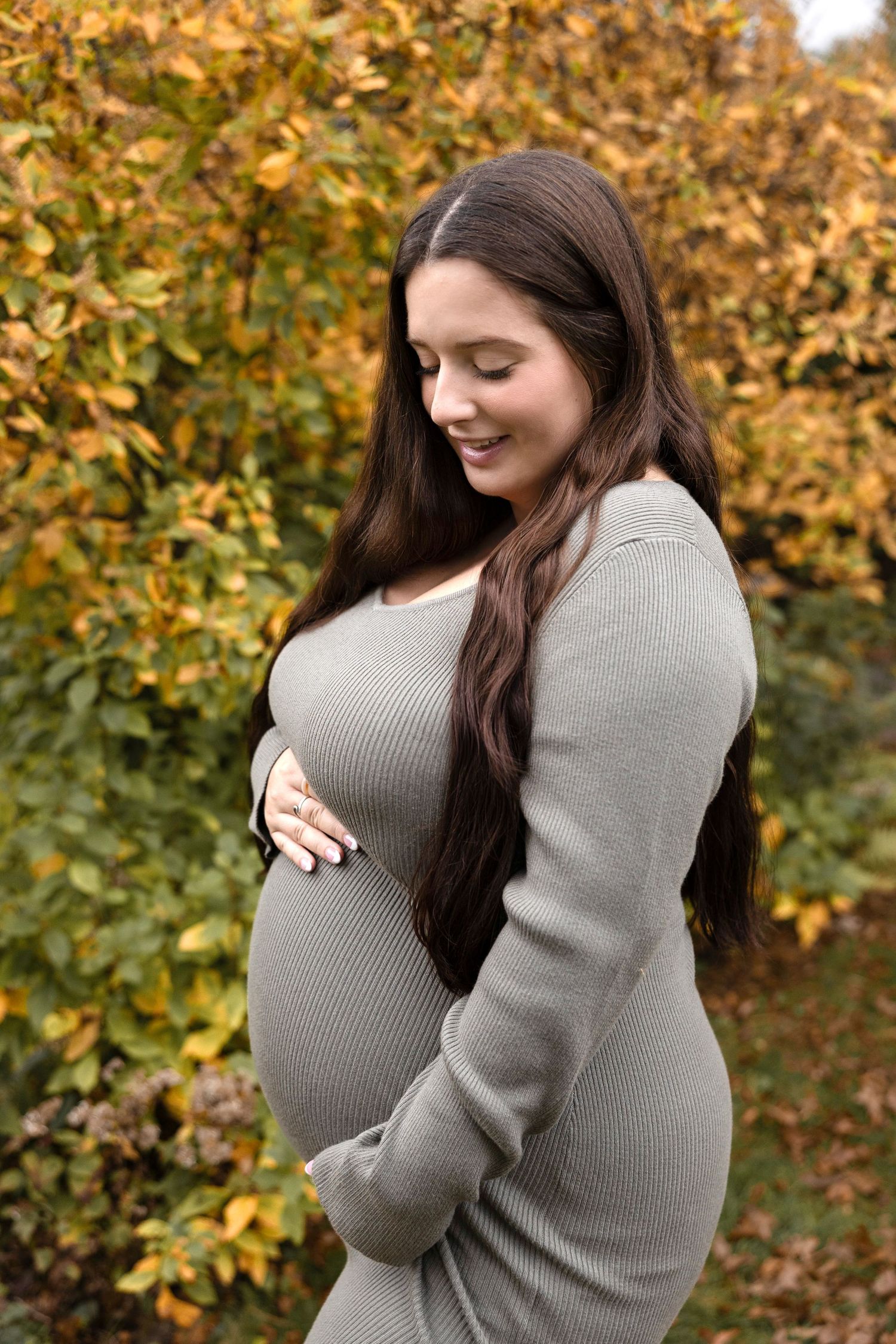 Maternity photoshoot in a park with warm autumn colors in the background.
