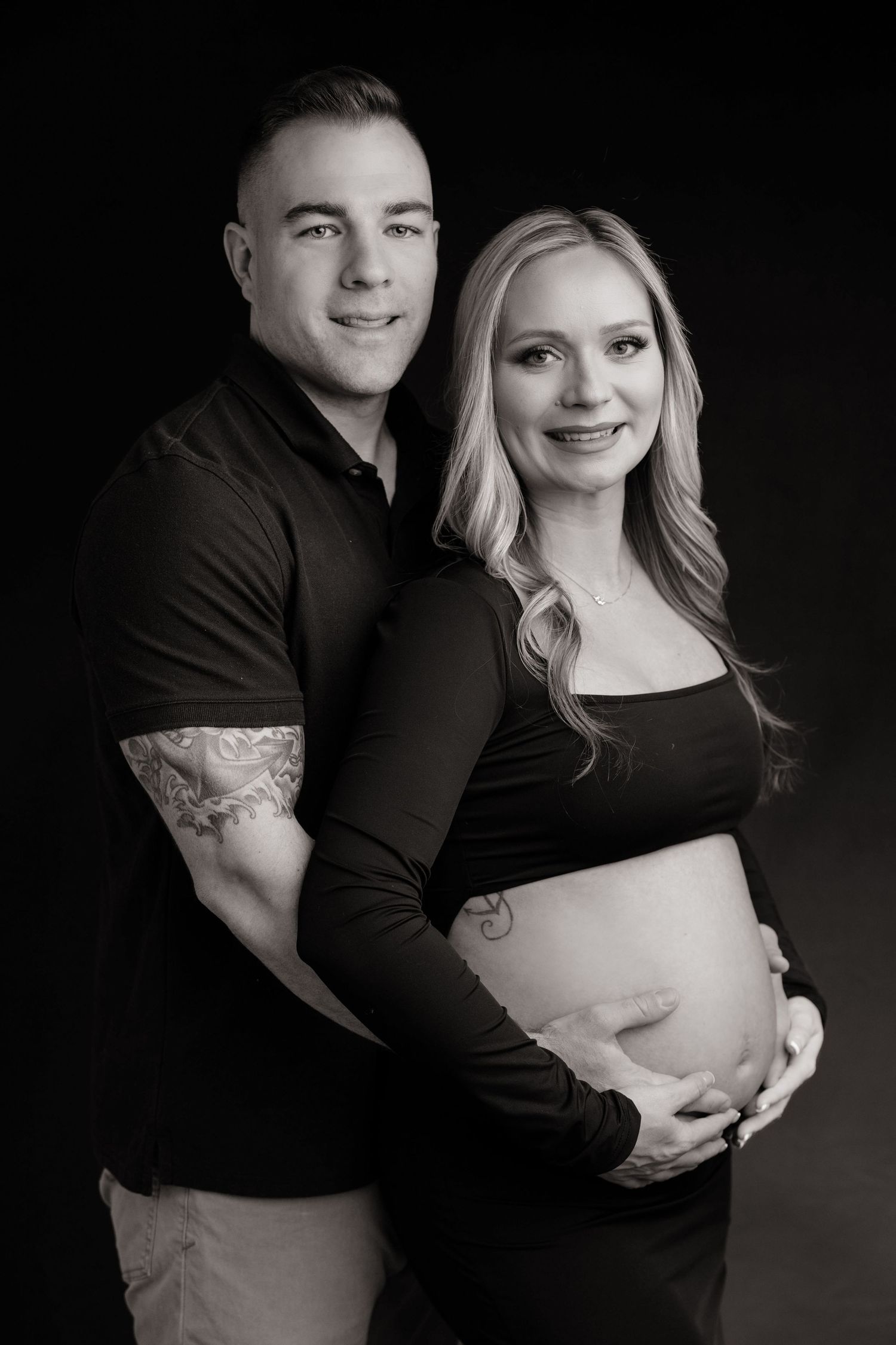Romantic maternity portraits showing couple embracing in dark studio setting.