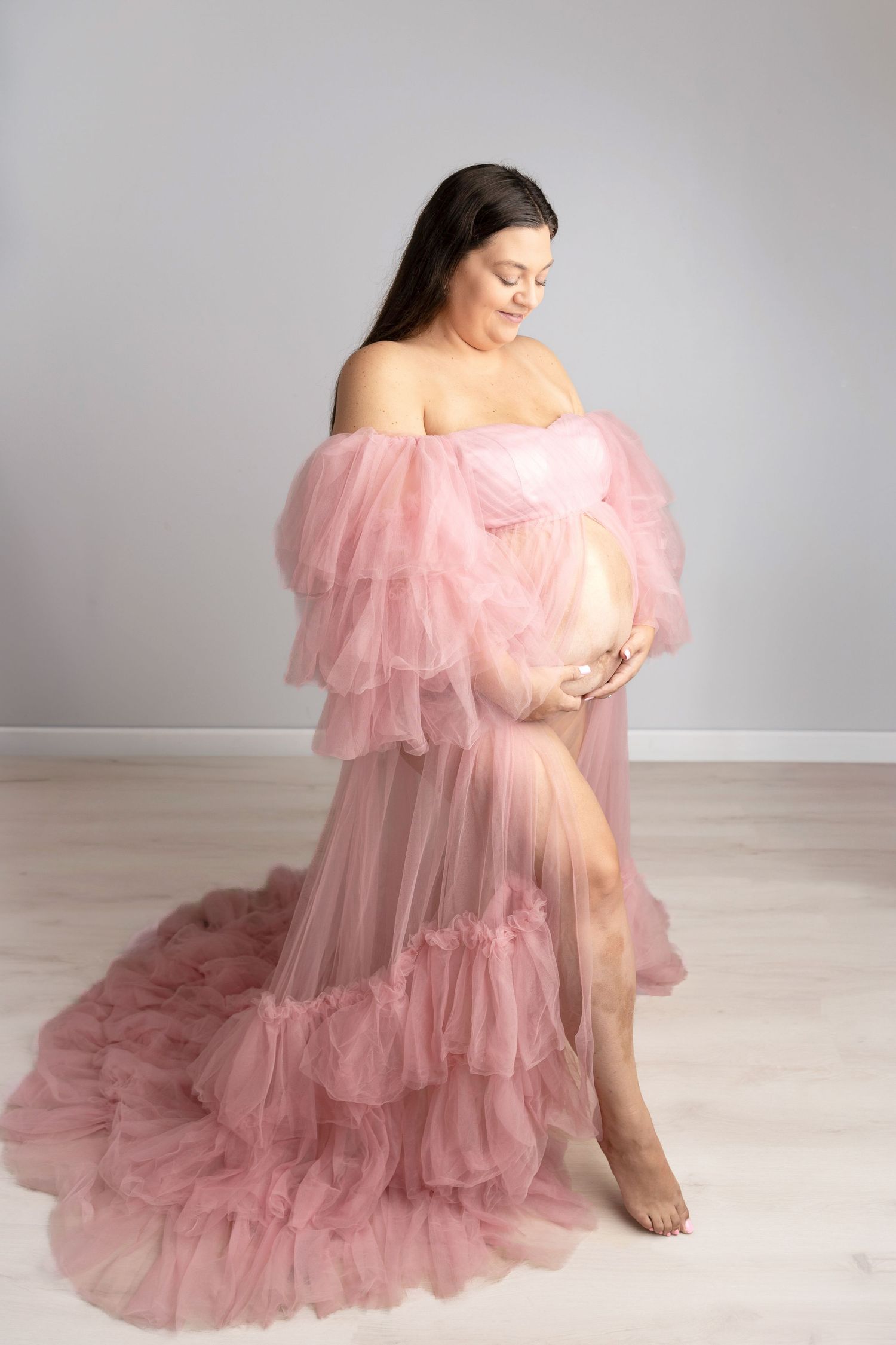 Maternity photos featuring flowing pink tulle dress against light grey background.