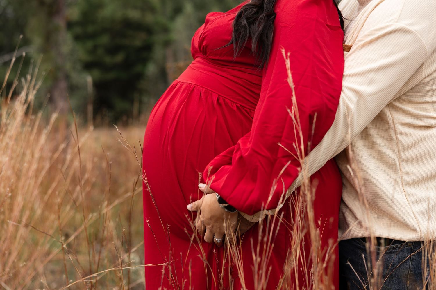 Couple embracing in a rustic field wearing red and cream colored outfits.