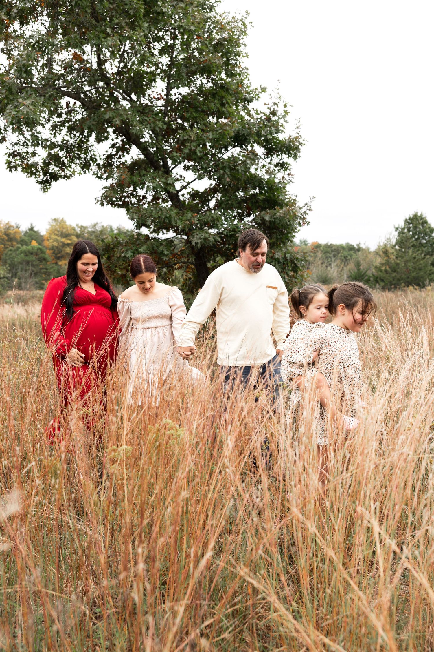 Family walking together through tall golden grass with trees in background.