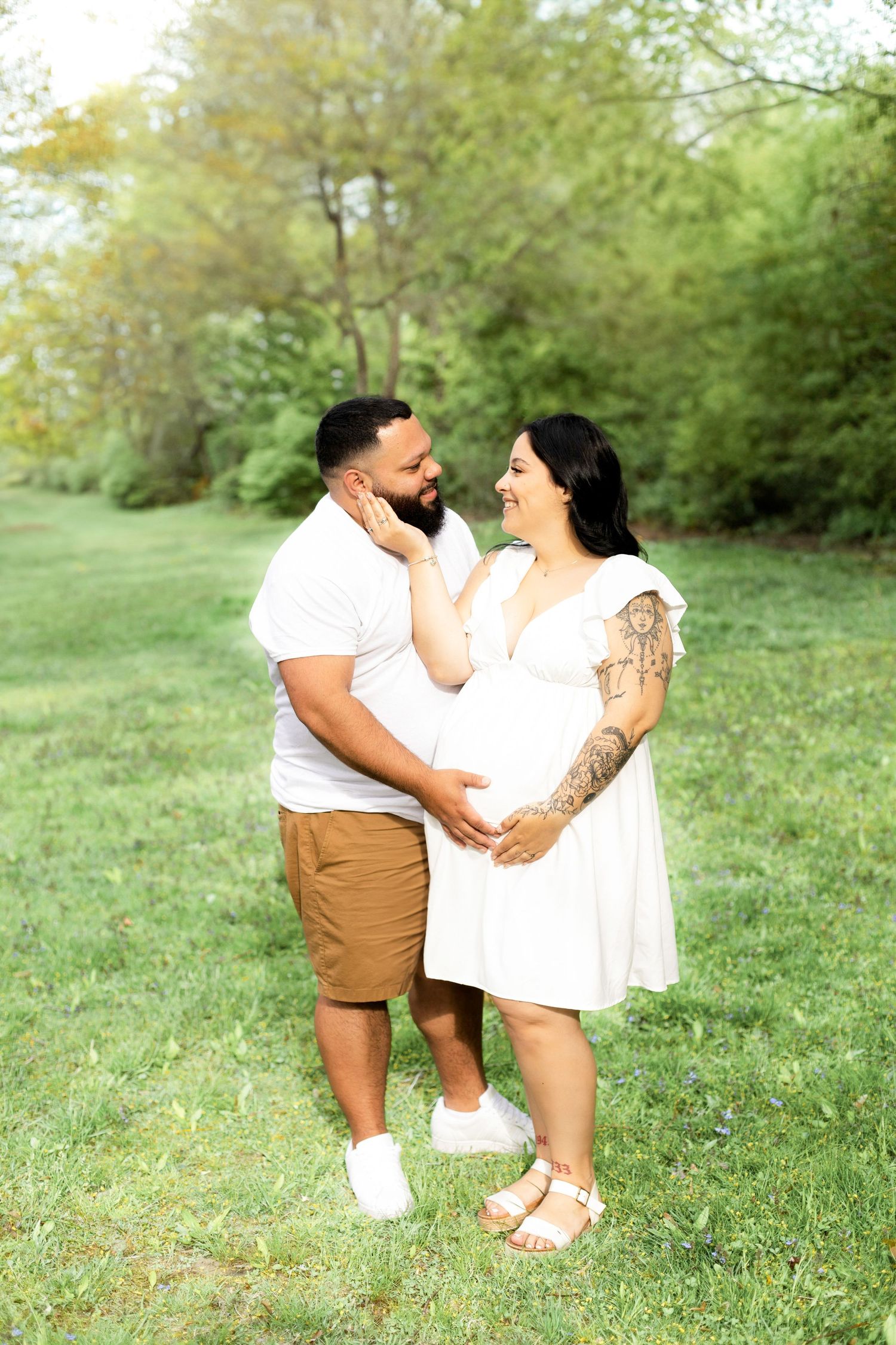 Couple embracing on grassy field in casual summer outfits.
