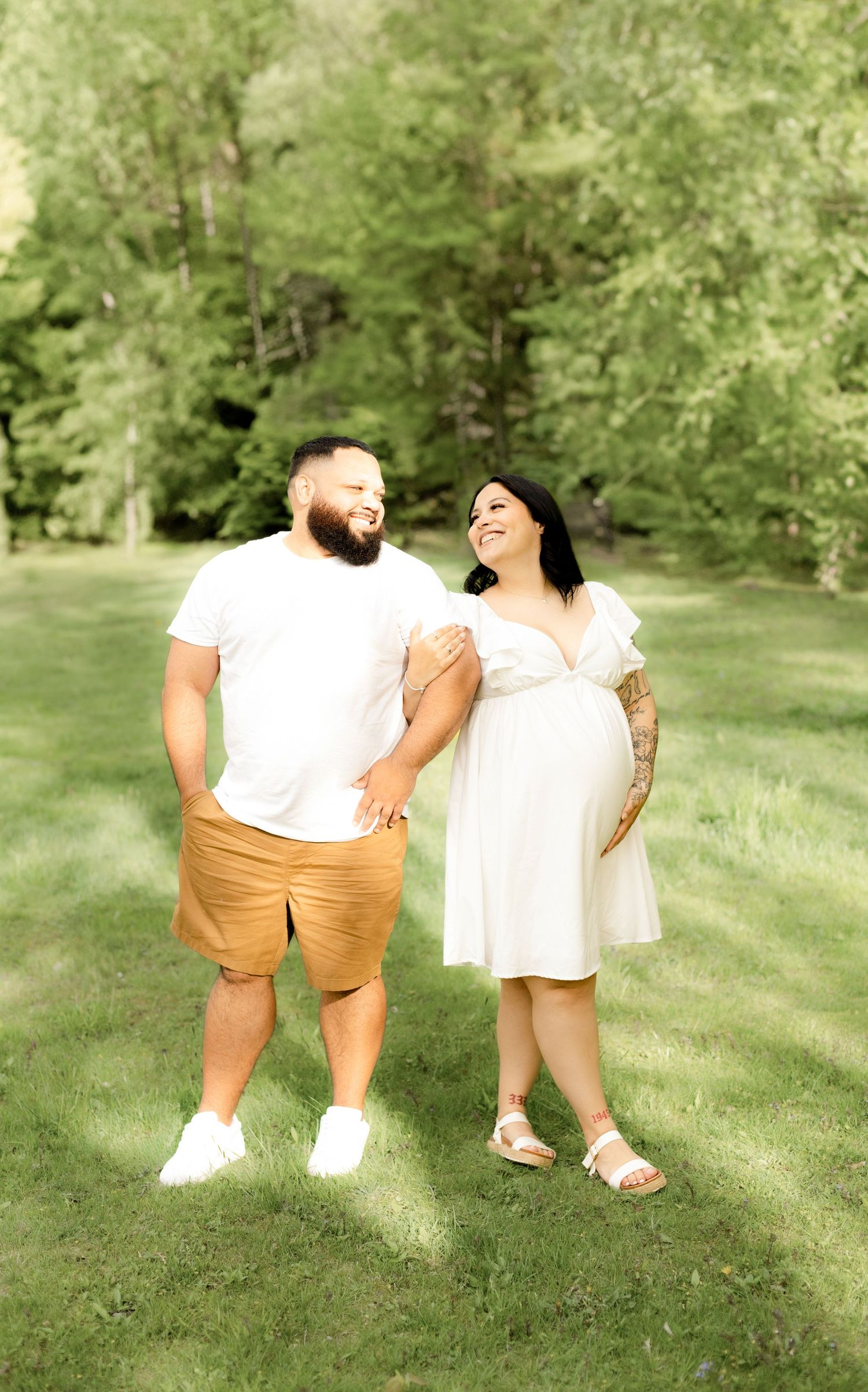 Couple sitting on grass in white and tan outfits during outdoor photo session.