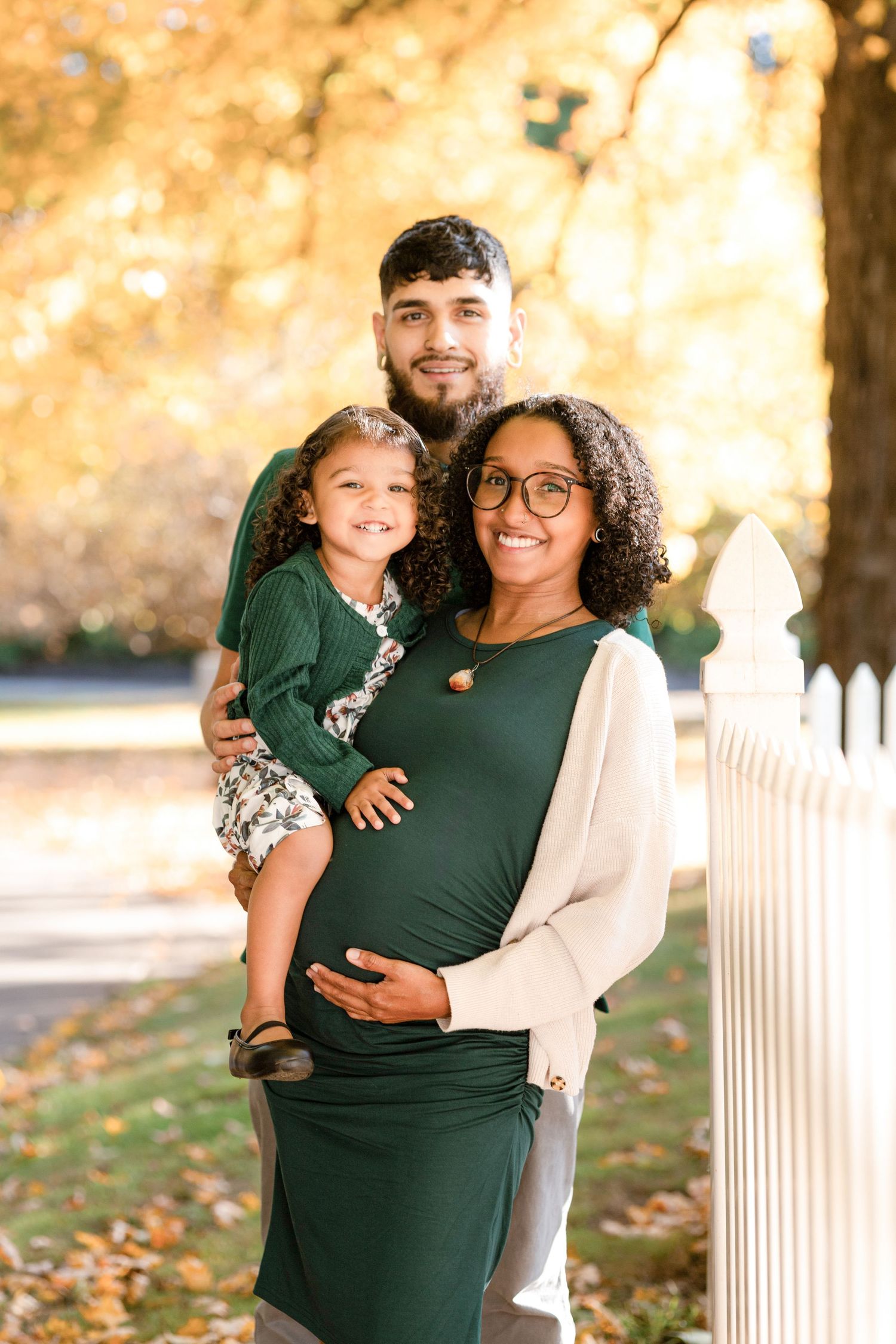 Family in coordinating green outfits poses together near white fence during autumn.