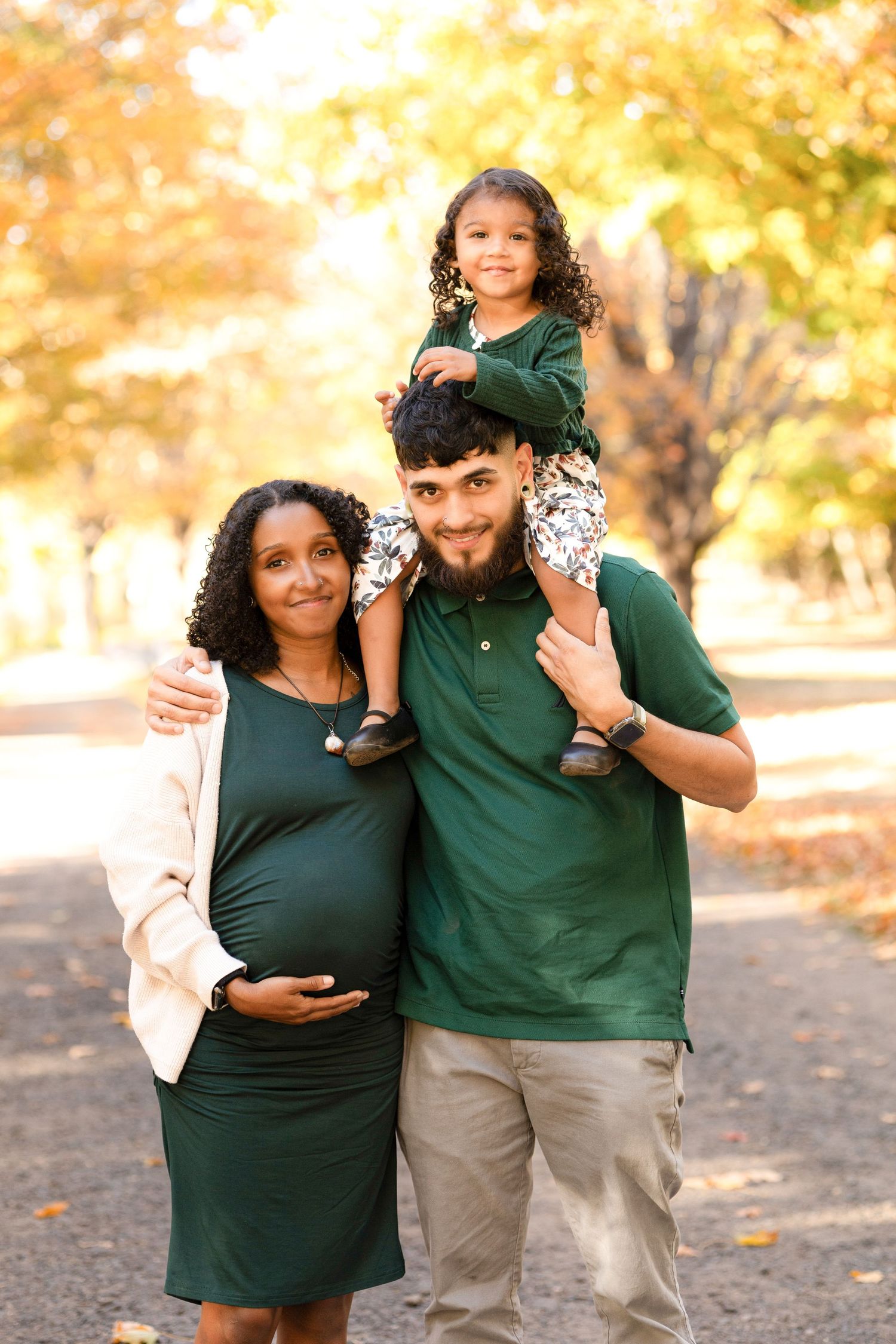 A family wearing green and khaki poses together outdoors during golden hour autumn photography session.
