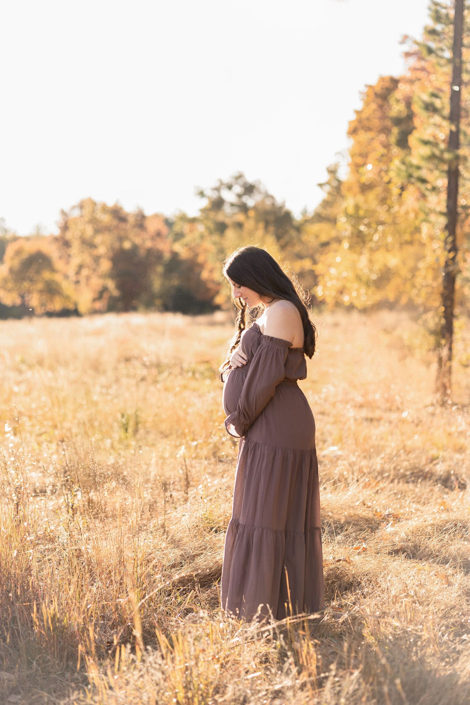 A woman in a mauve dress stands thoughtfully in a sunlit autumn field.
