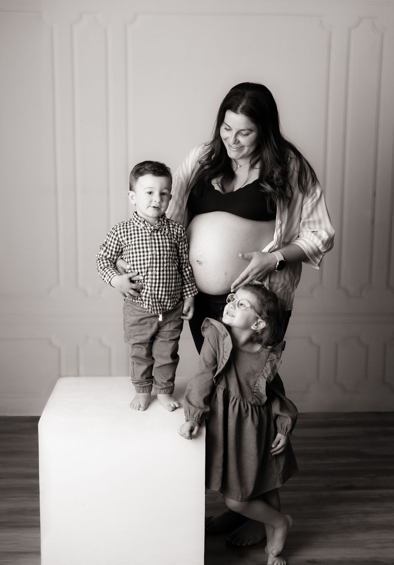 Black and white family portrait series with a white cube prop in a minimalist setting.