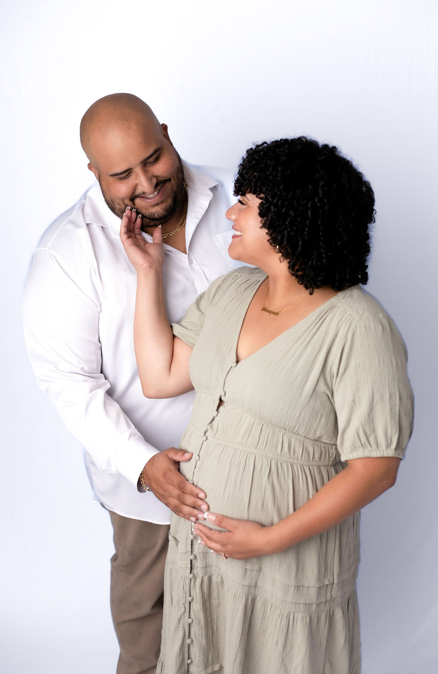 Maternity photo session with couple in neutral tones against white background.