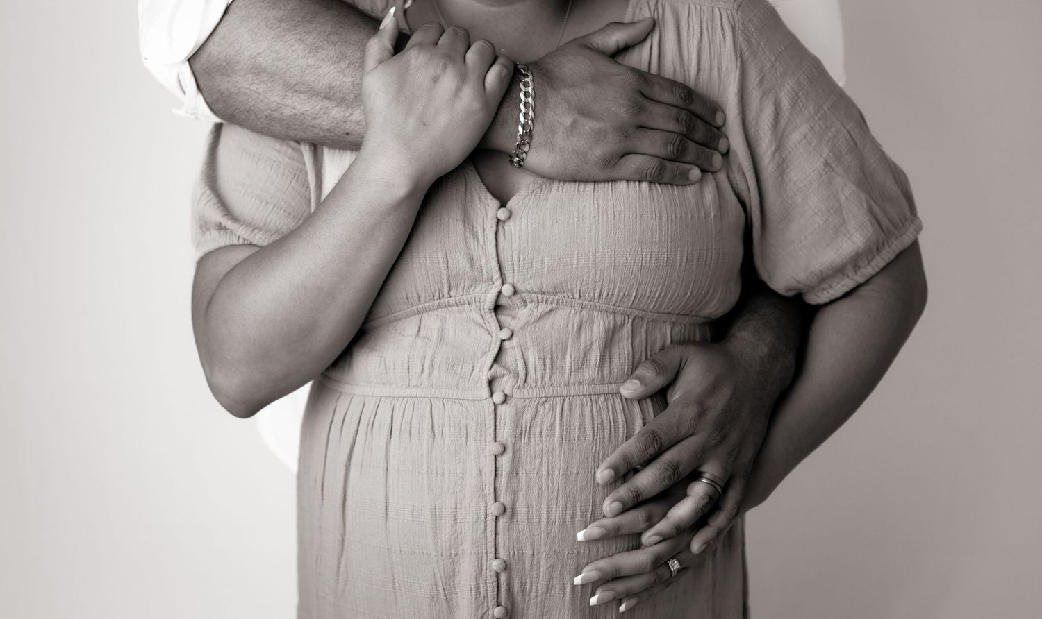 Artistic maternity photoshoot in a light beige dress against a white studio backdrop.