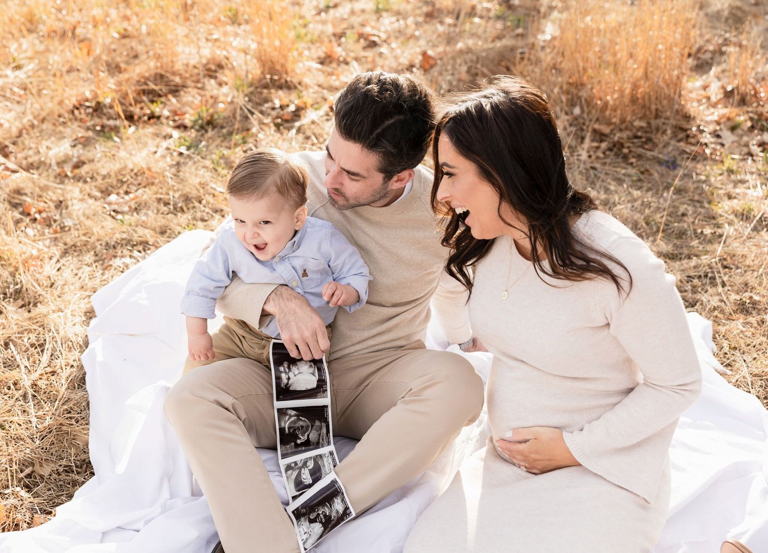 Maternity photography session showing loving family moments on white blanket outdoors.