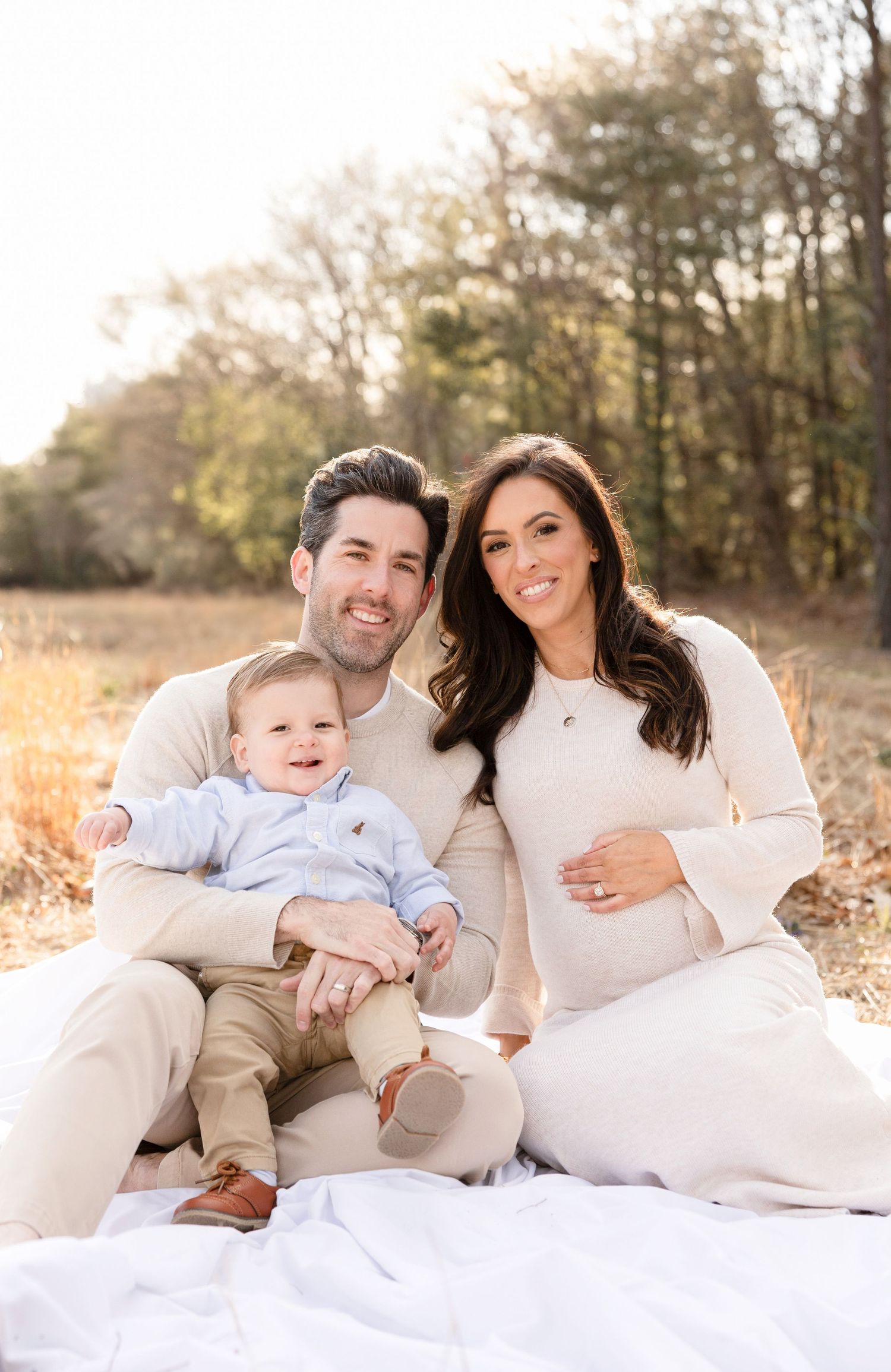 Family shares tender moments during outdoor maternity photo session on white blanket.