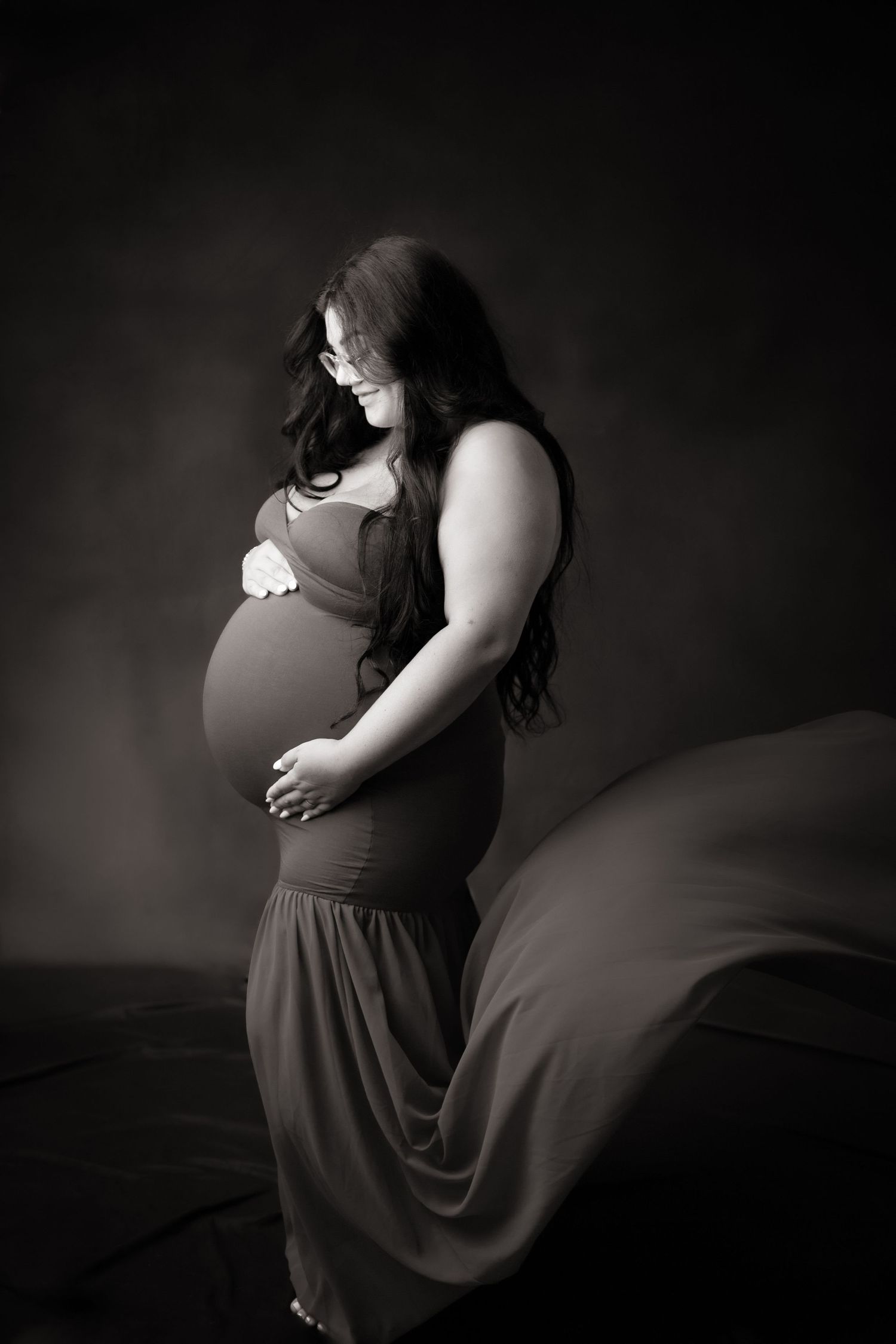Artistic black and white maternity portrait showing expectant mother in flowing dress.
