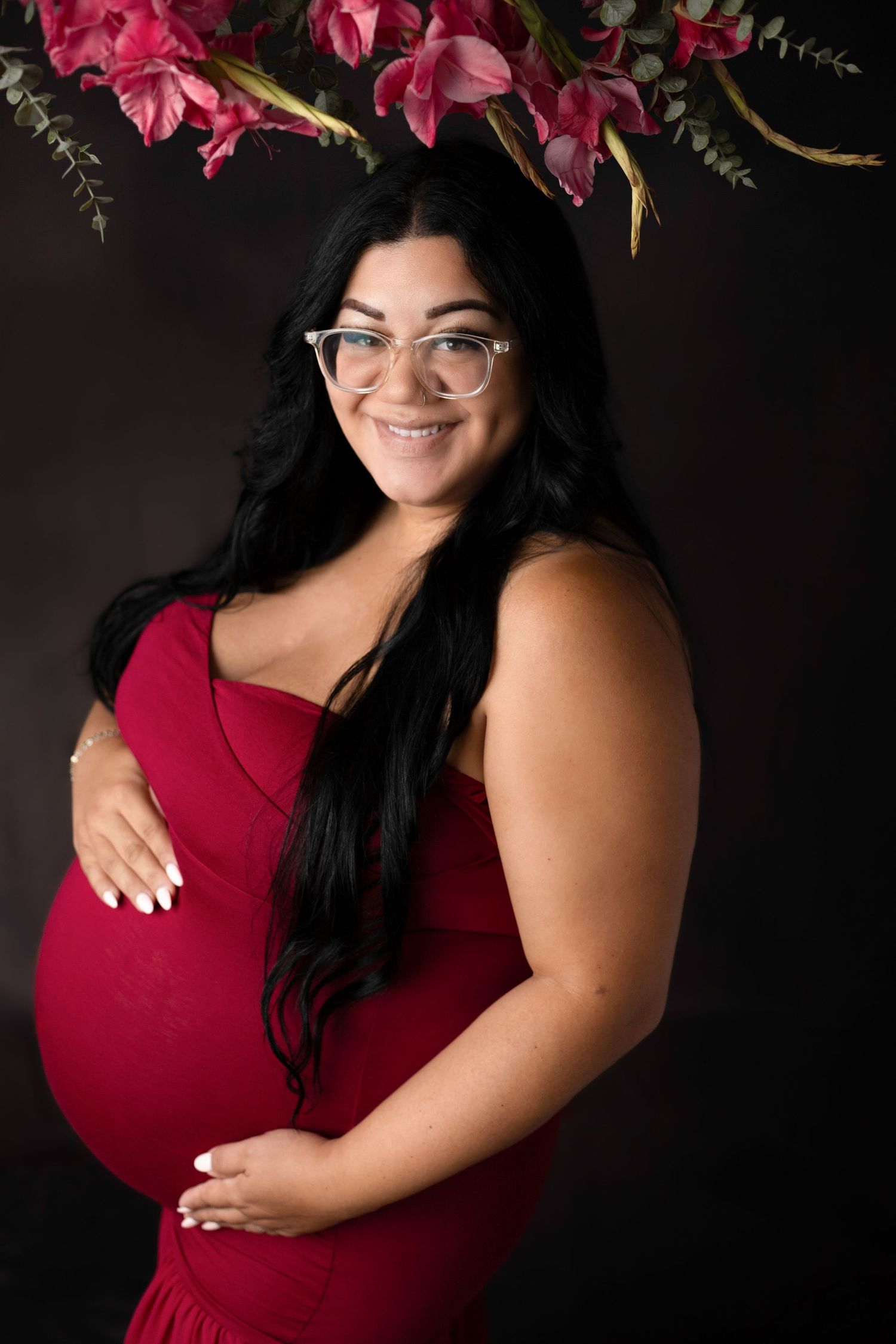 Maternity portrait with pink flowers featuring expectant mother in red dress.