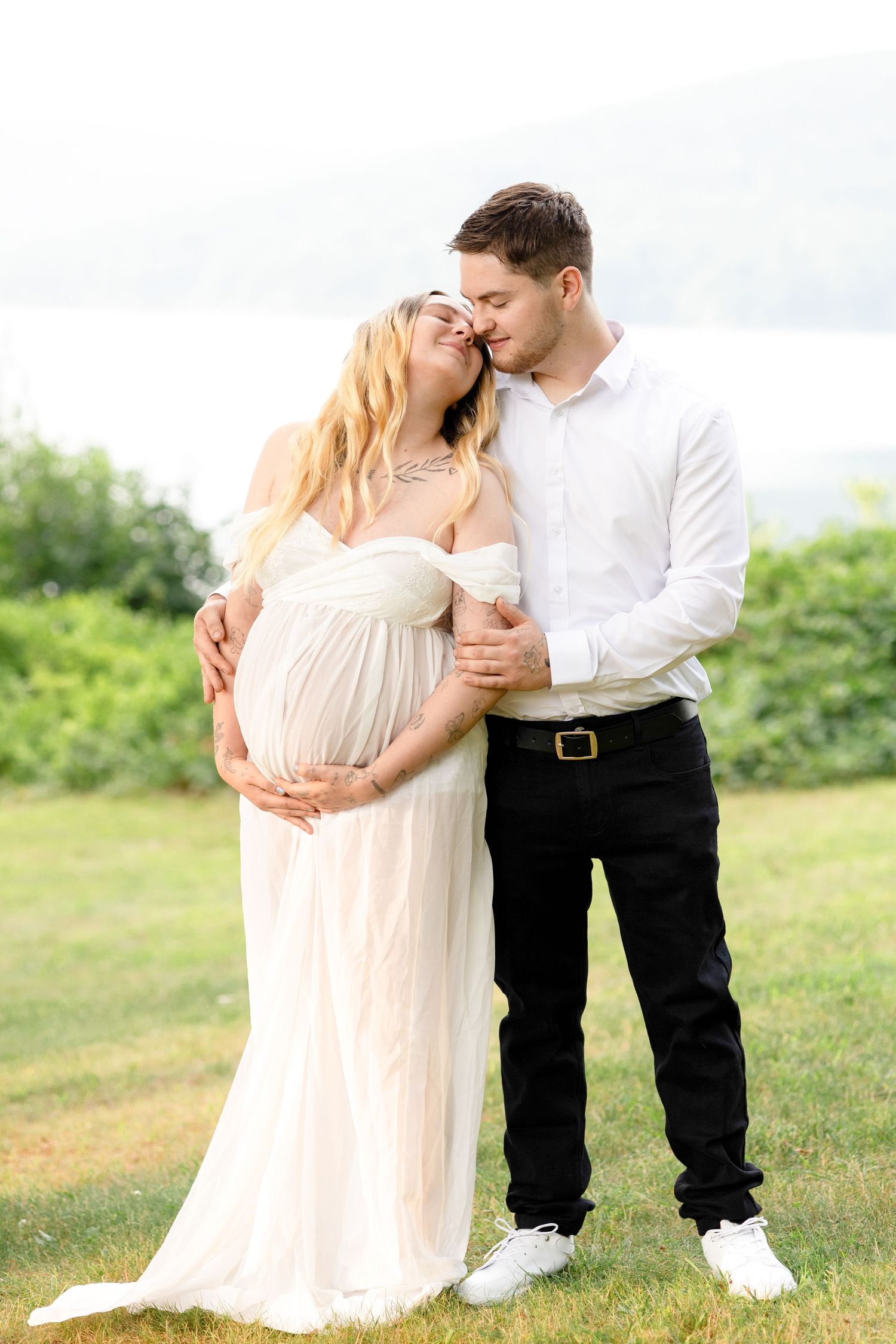 Romantic couple in white and black outfits embracing in sunny meadow.