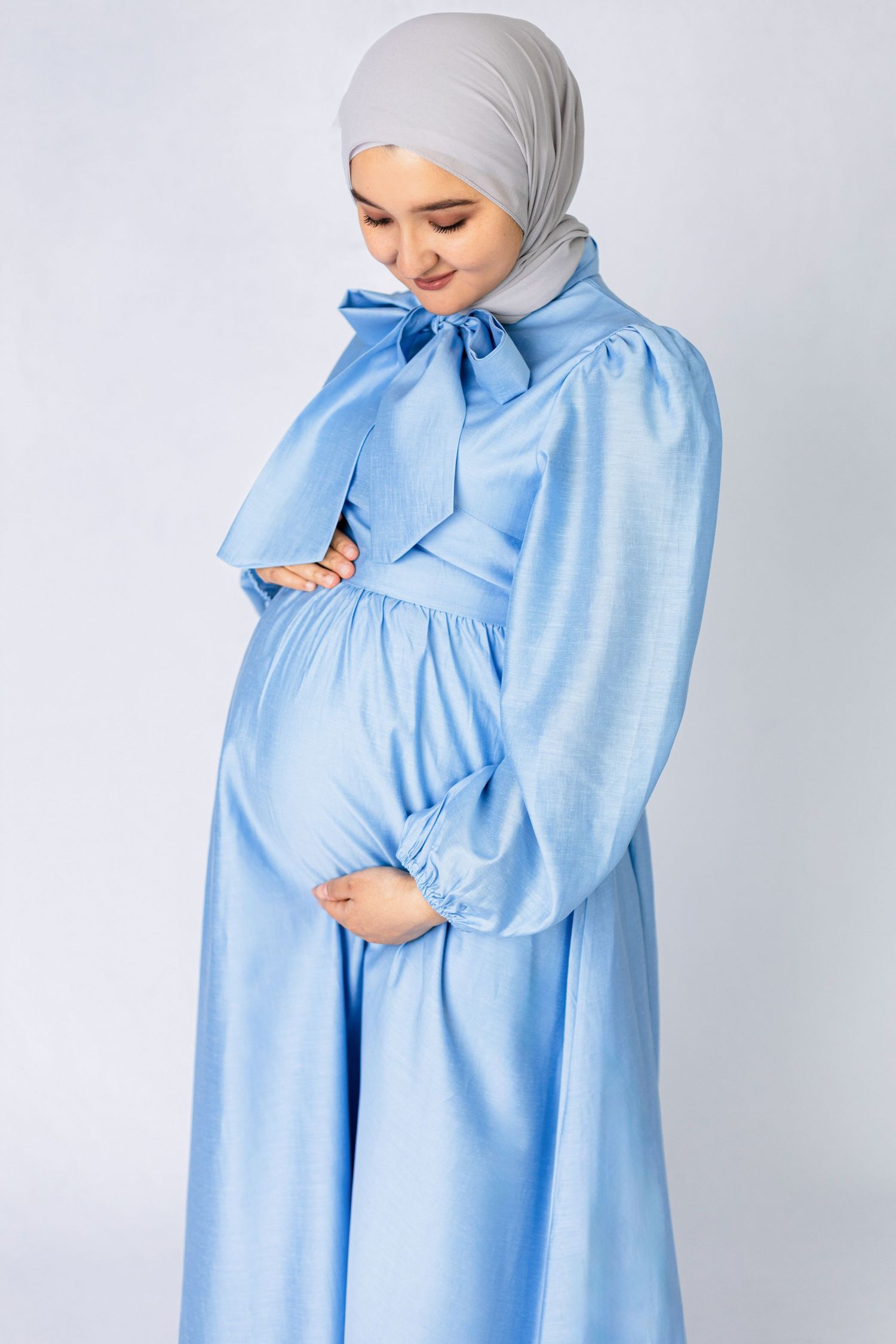 Woman in light blue modest dress with bow detail against white background.
