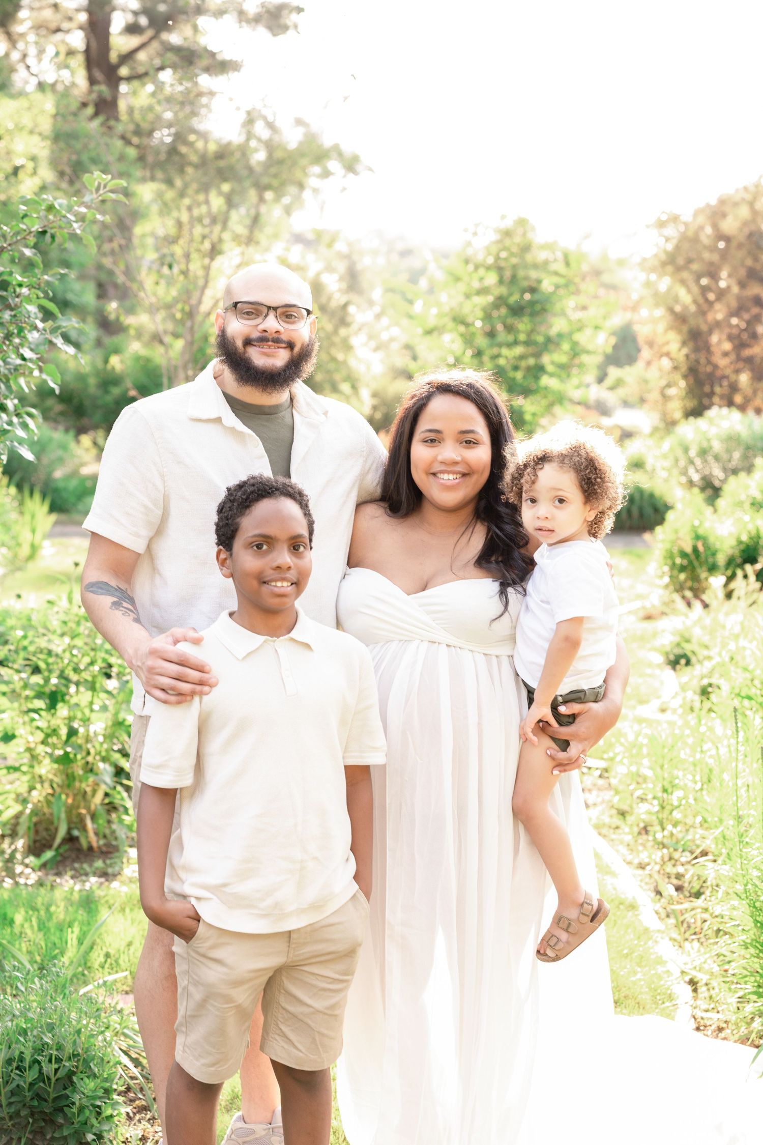 Family portrait in sunny garden setting wearing coordinated white and neutral outfits.