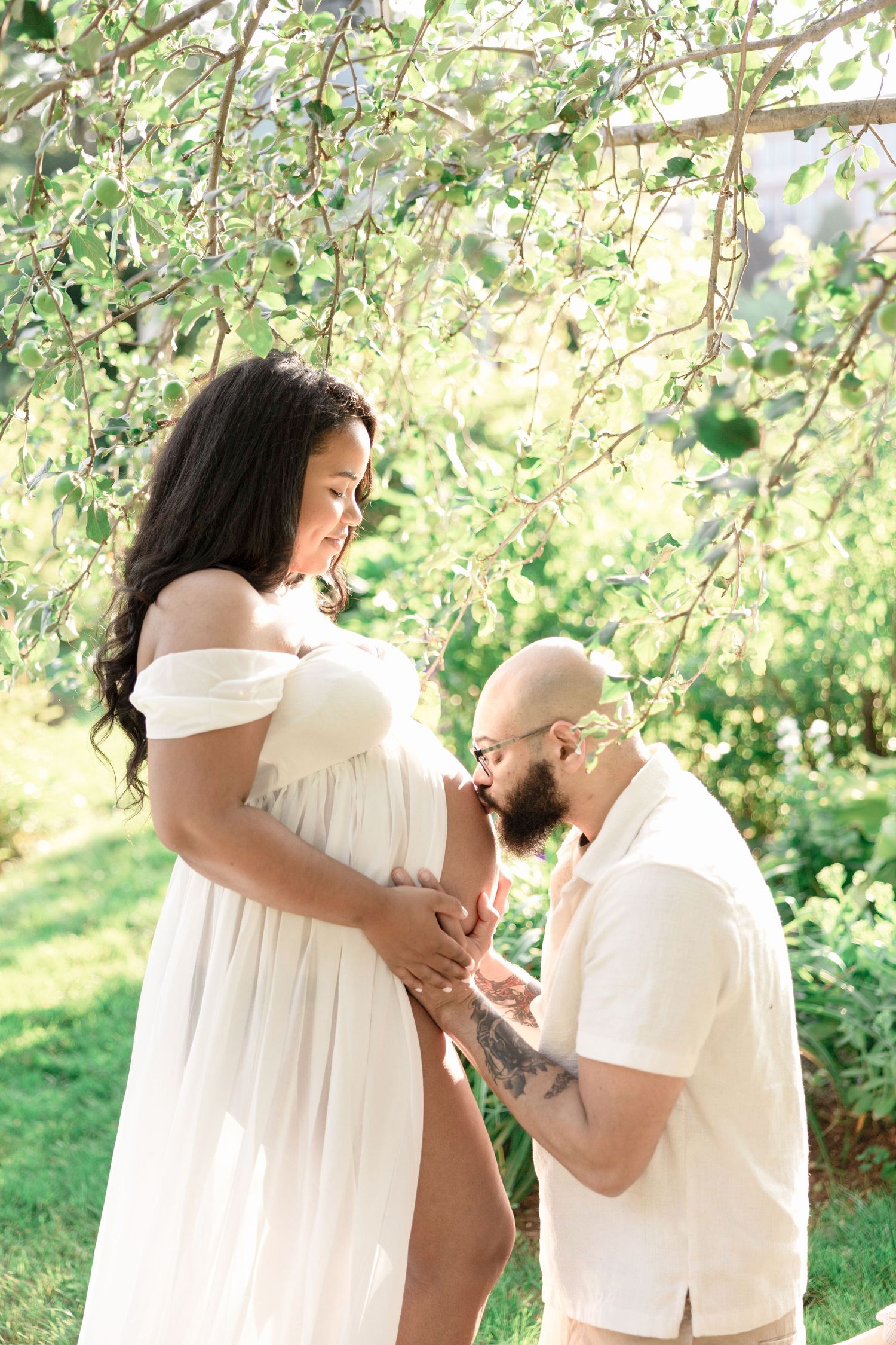 A couple in white outfits shares intimate moments in a garden setting with green foliage.