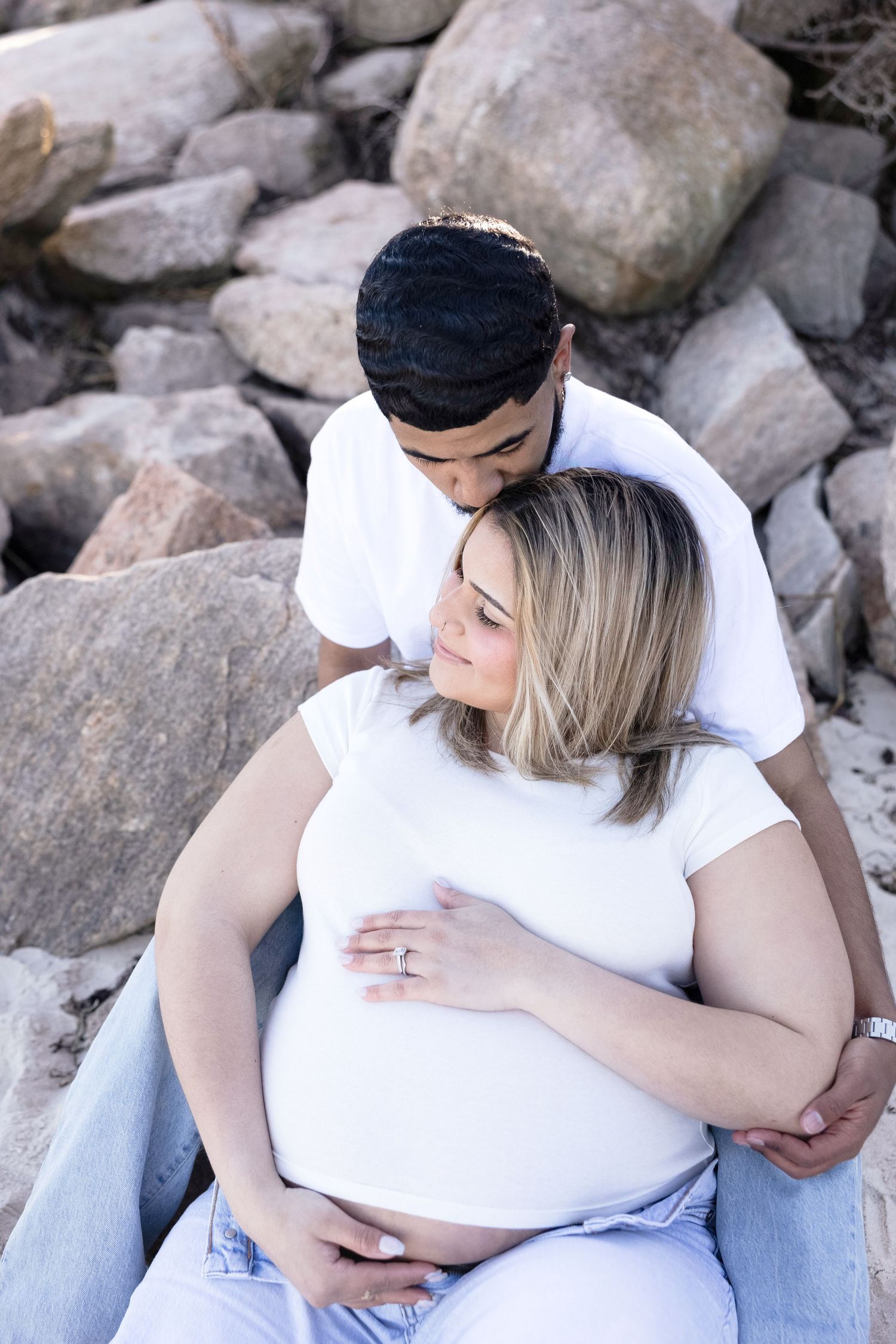 Couple in casual wear sits intimately among rocky terrain.