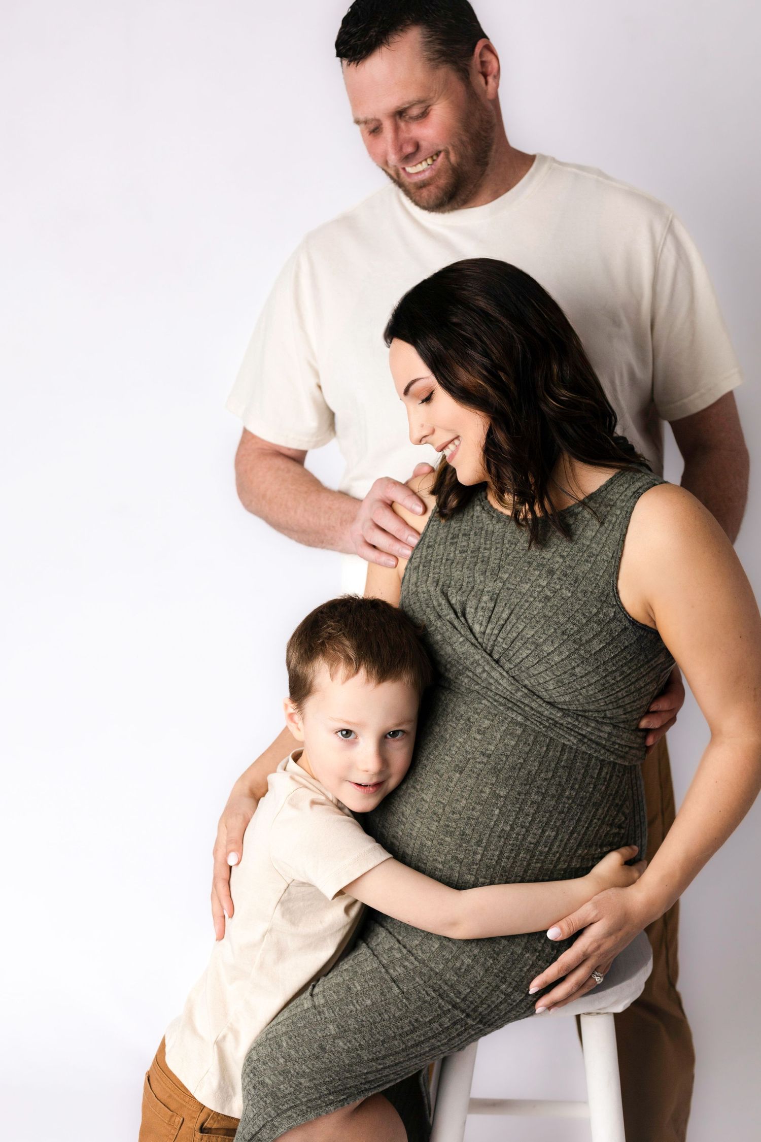 Maternity portrait of expecting family embracing against white background.