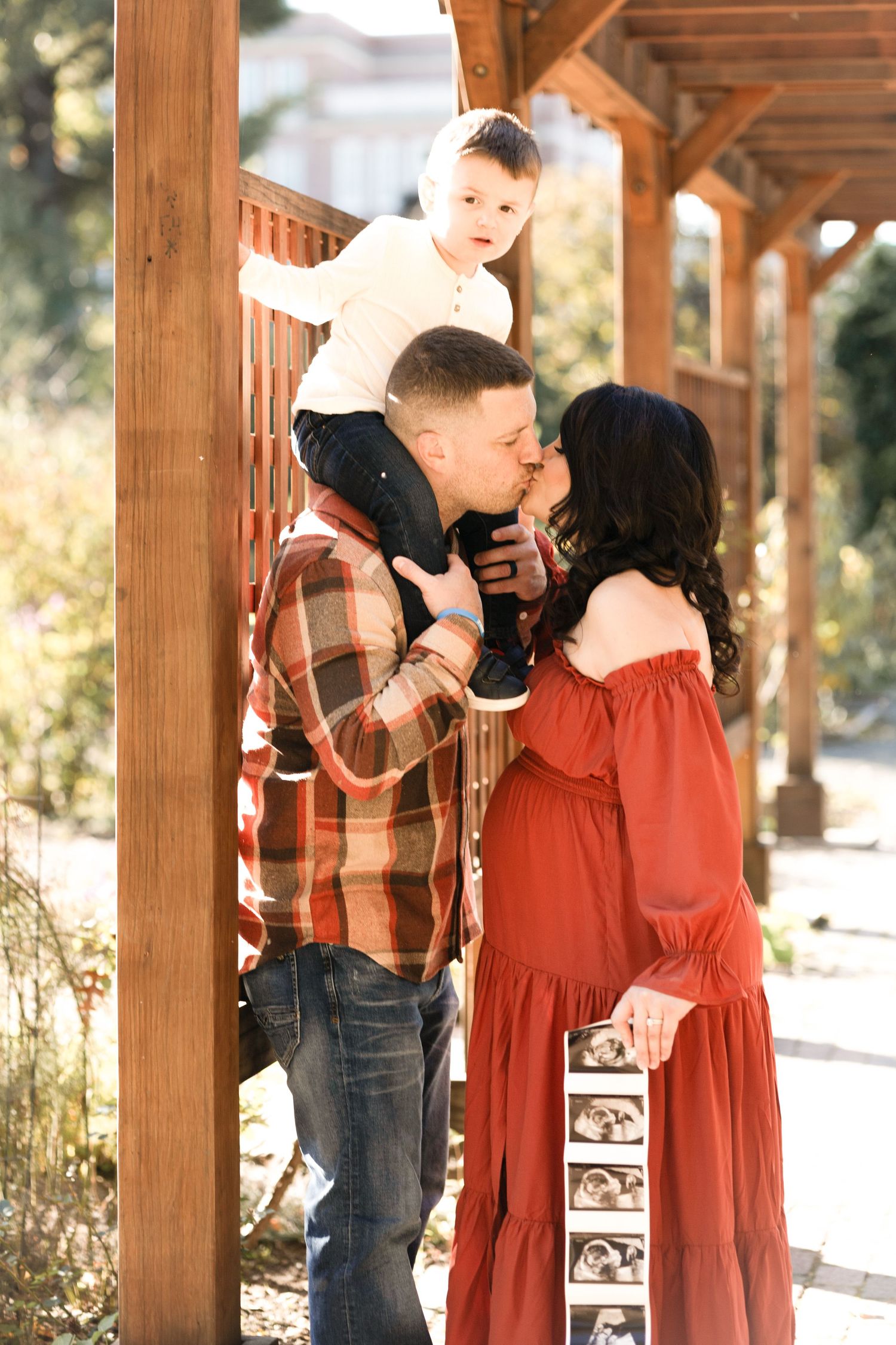 A family shares intimate moments under a wooden pergola during an outdoor photo session.