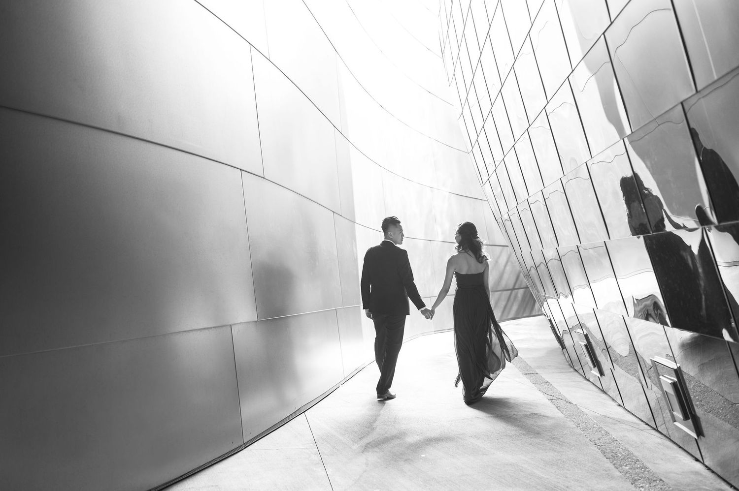 Artistic black and white silhouette of a couple holding hands in a modern architectural corridor.