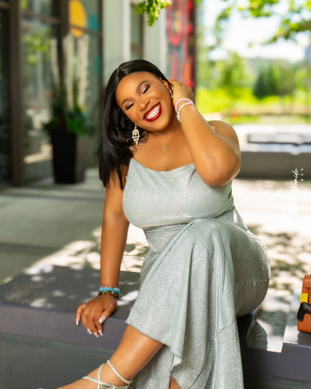 A woman in a silver dress laughs joyfully while posing outdoors.