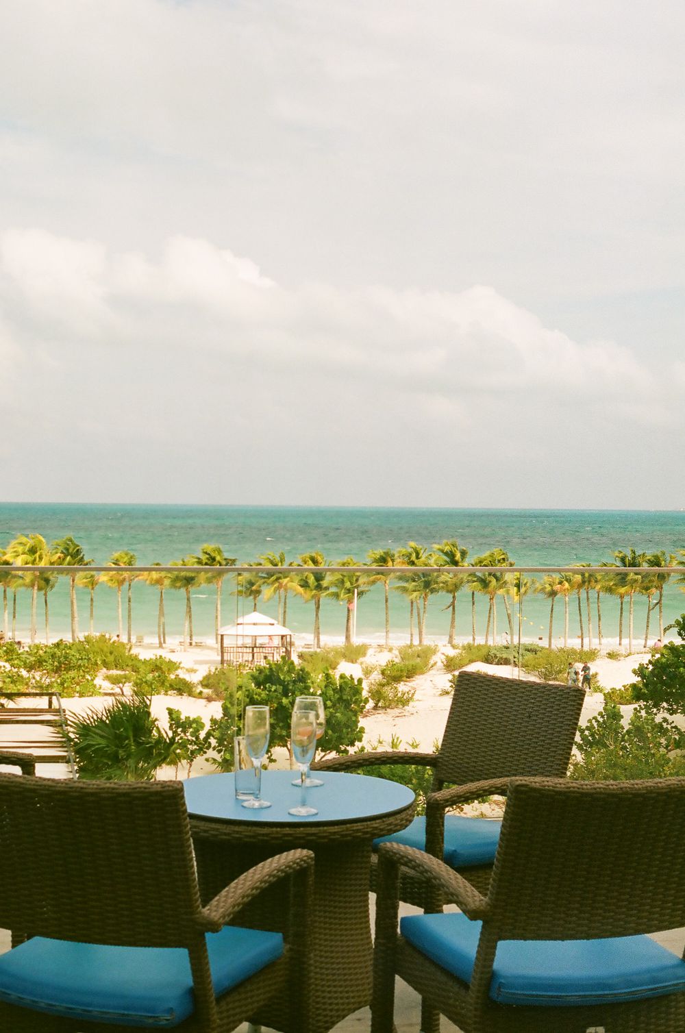 Beachfront seating area with wicker chairs overlooking palm trees and turquoise ocean waters.