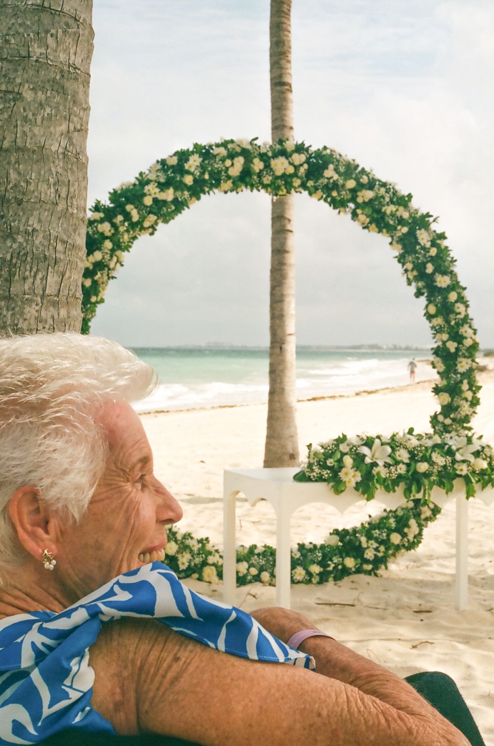Floral wedding arch decorates a beachside ceremony setup with white chairs and ocean views.